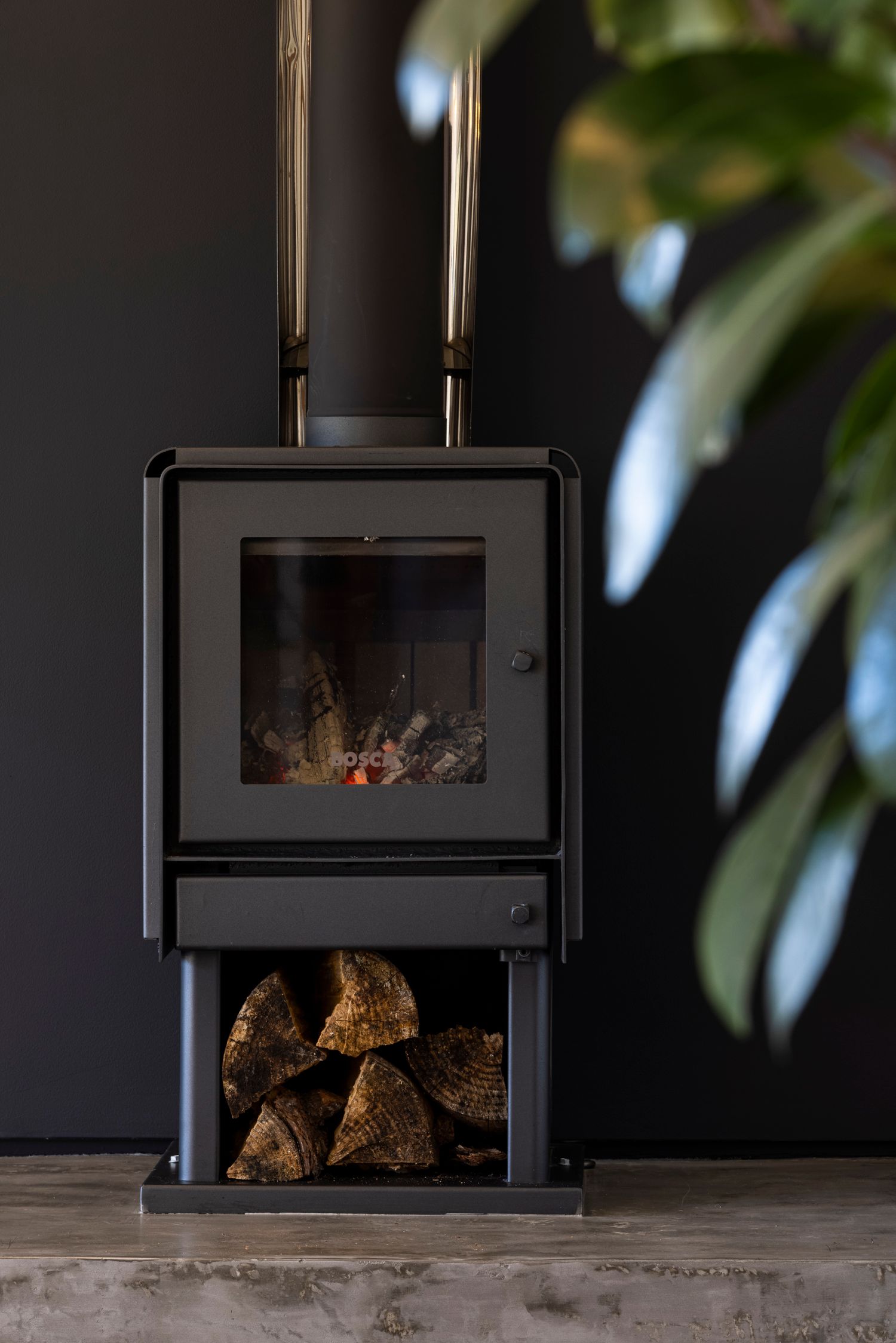 Modern black wood burning stove with stacked firewood storage underneath.