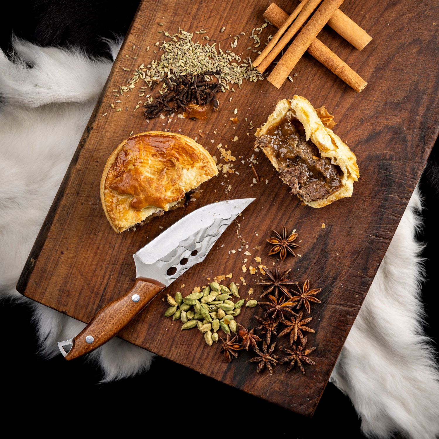 Spices and star anise scattered on wooden cutting board next to kitchen utensils.