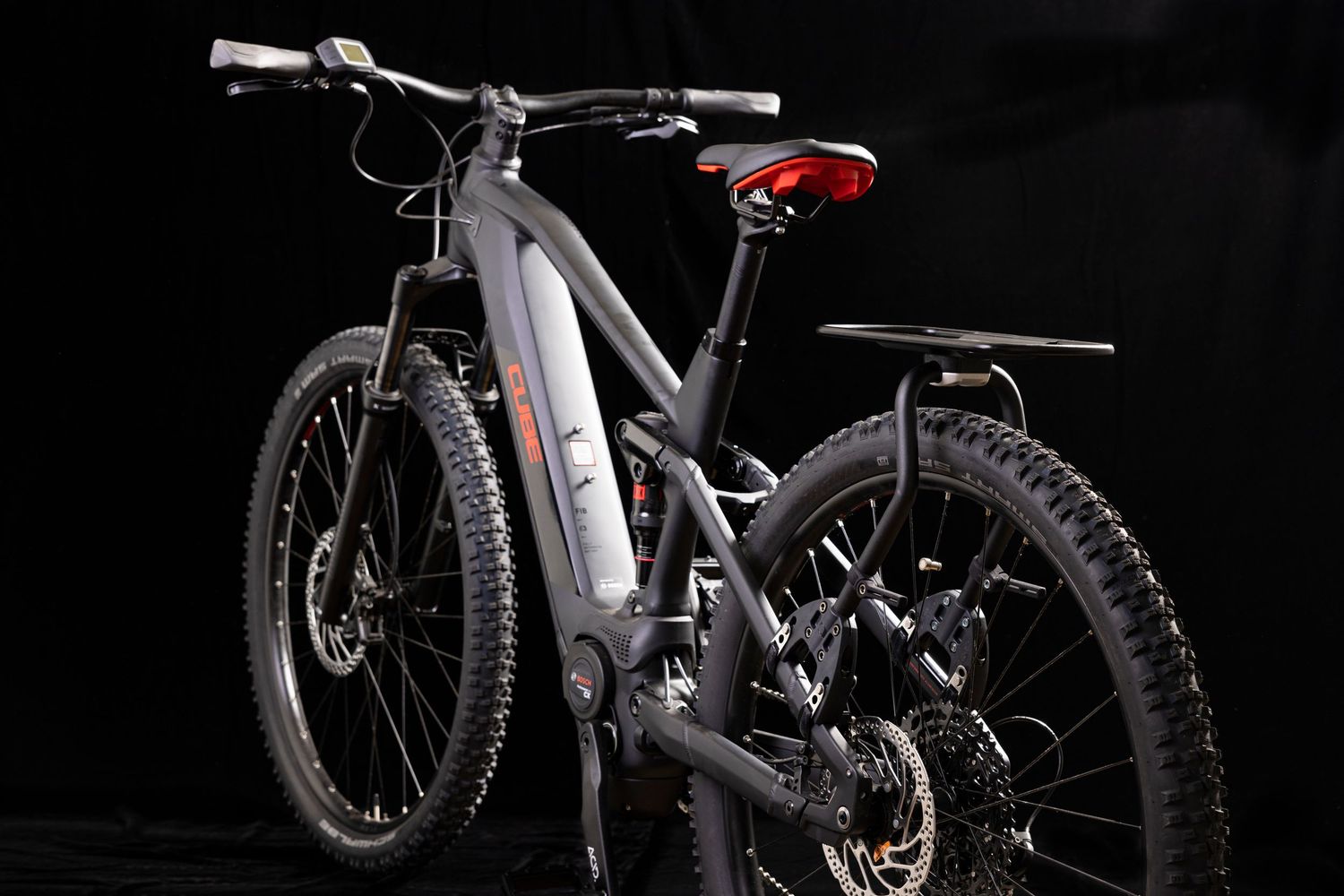 Modern mountain bike with black frame and red seat photographed against dark background.
