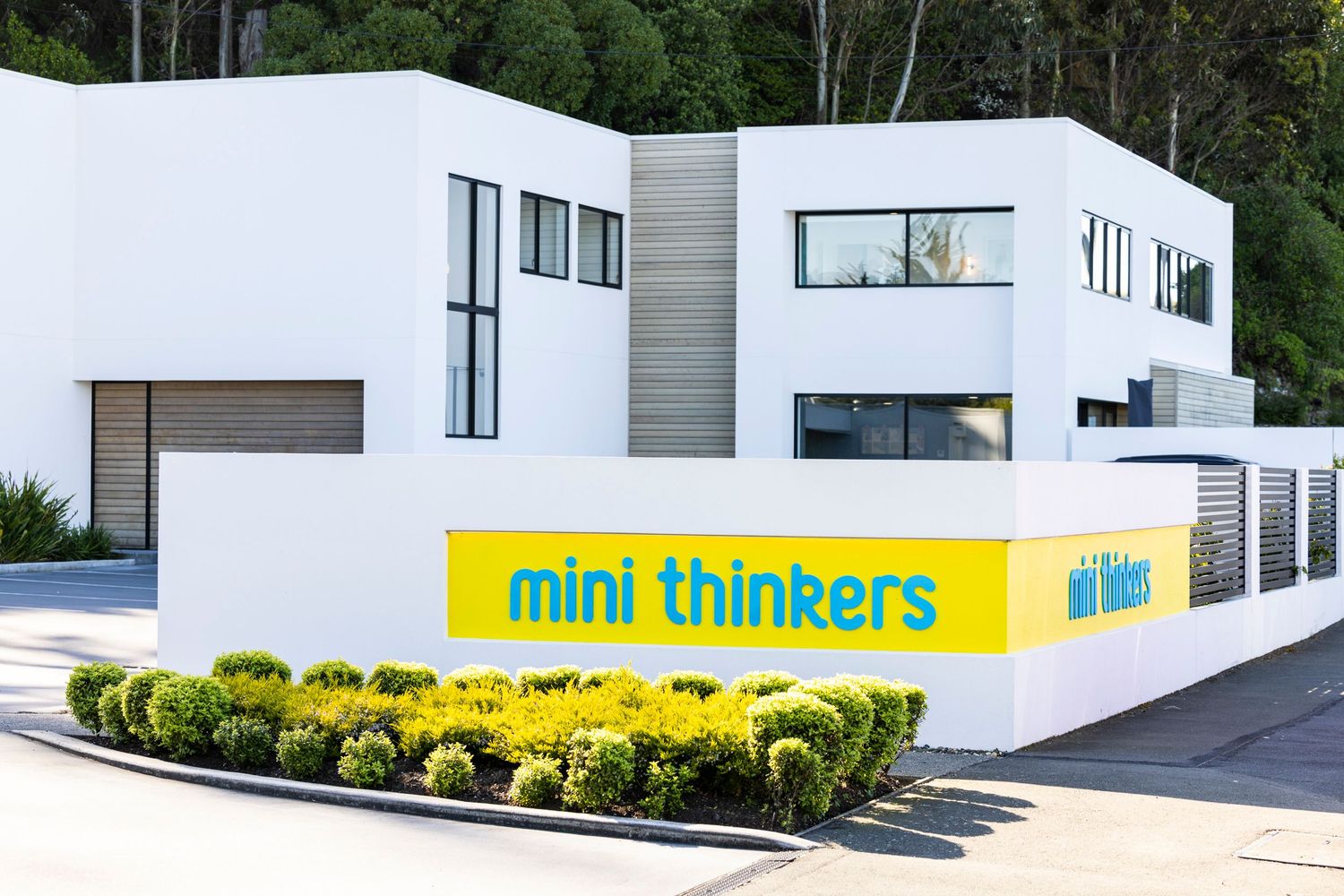 Modern white commercial building with yellow Mini Thinkers sign and landscaped entrance.