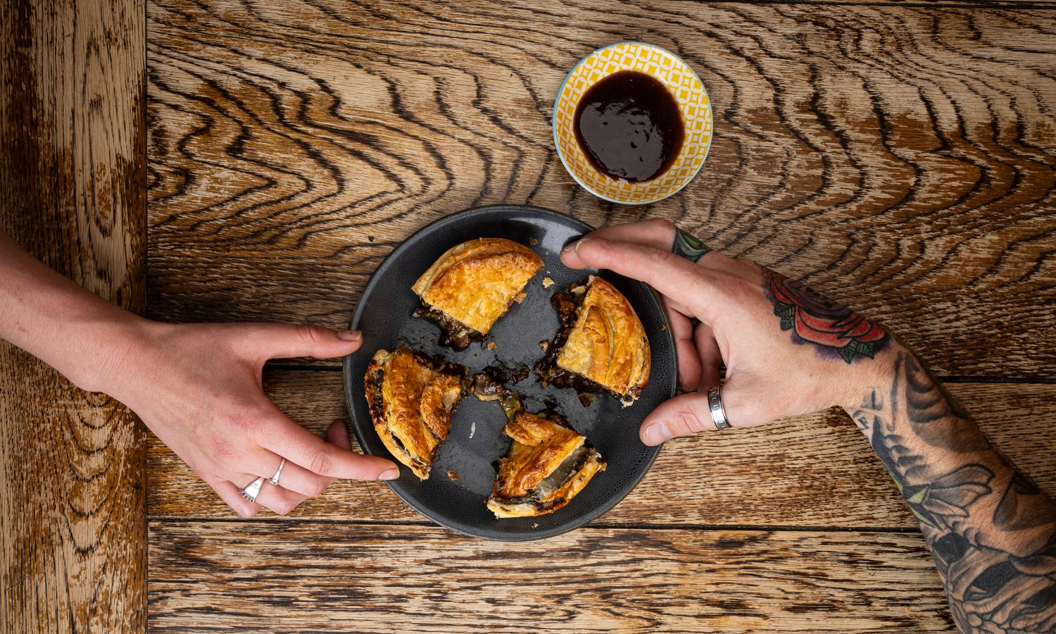 Step by step process of crumbly dough being pressed into a dark-colored tart pan on a wooden surface.
