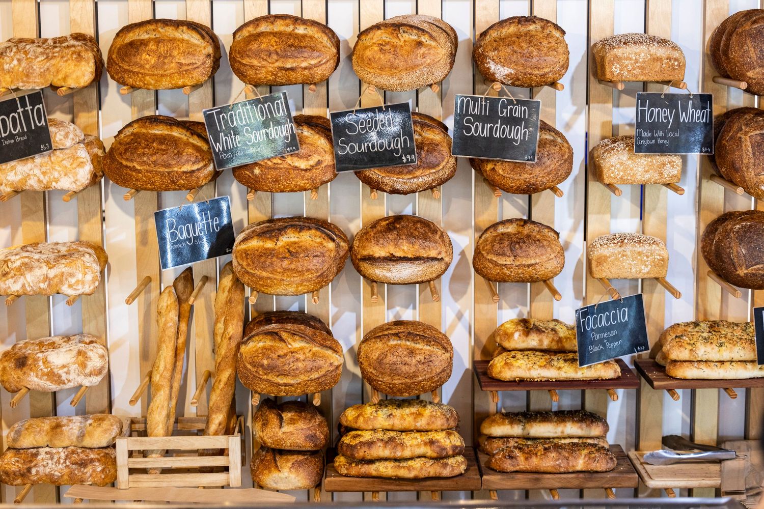 Display of artisanal breads and baguettes with handwritten labels on wooden shelving.