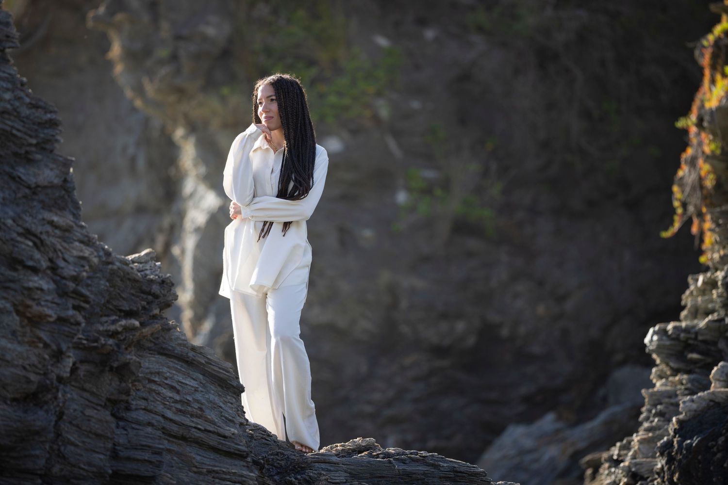 Person in white outfit standing contemplatively on rocky cliff edge.