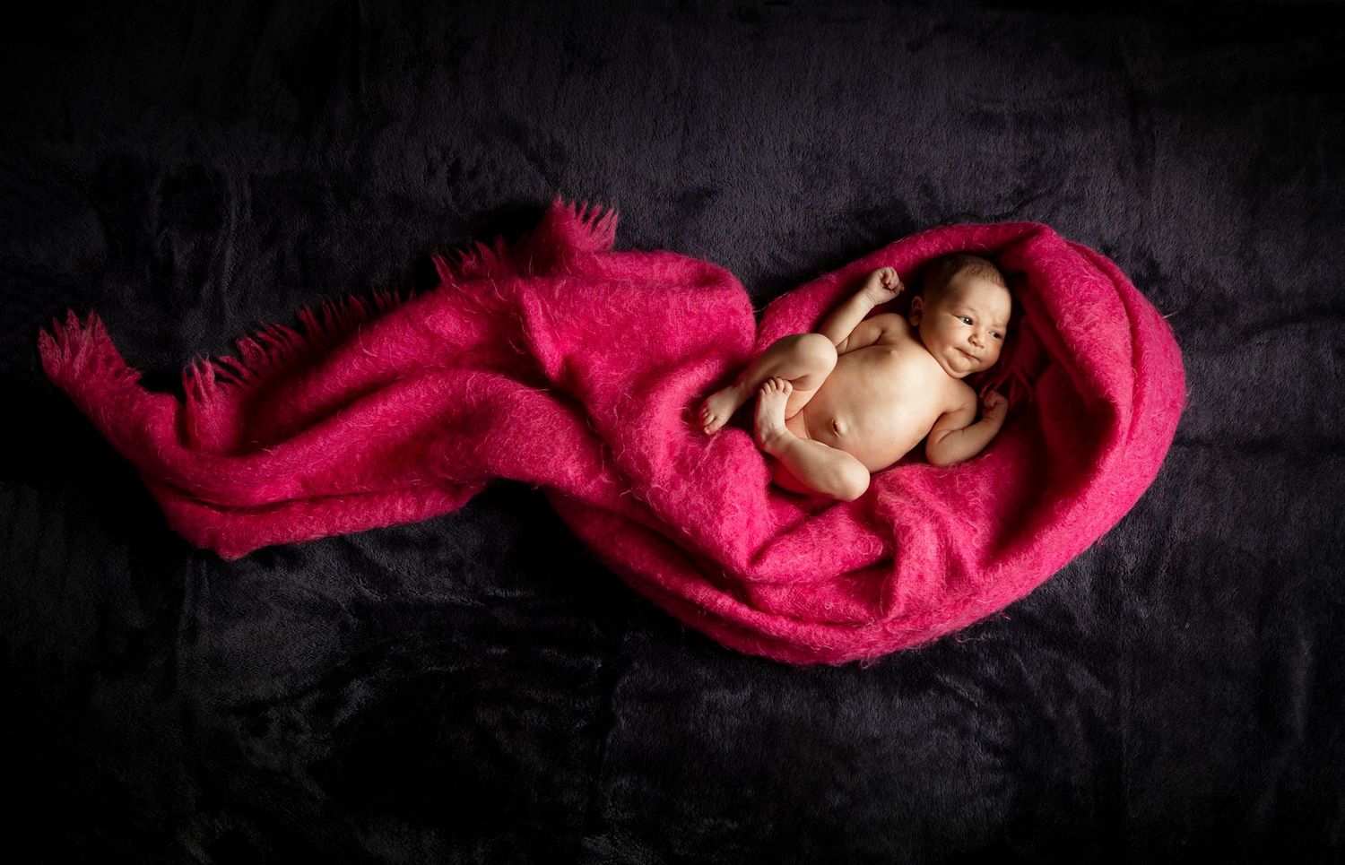 Artistic newborn photography series featuring a baby wrapped in vibrant red fabric against black background.