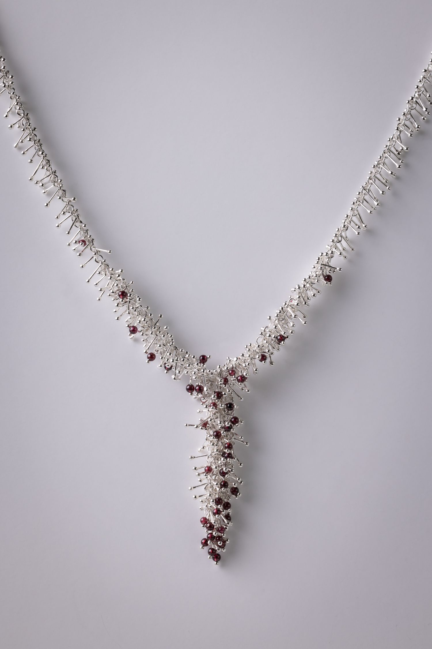 Luxurious Y-shaped silver necklace adorned with red stones displayed on light grey background.