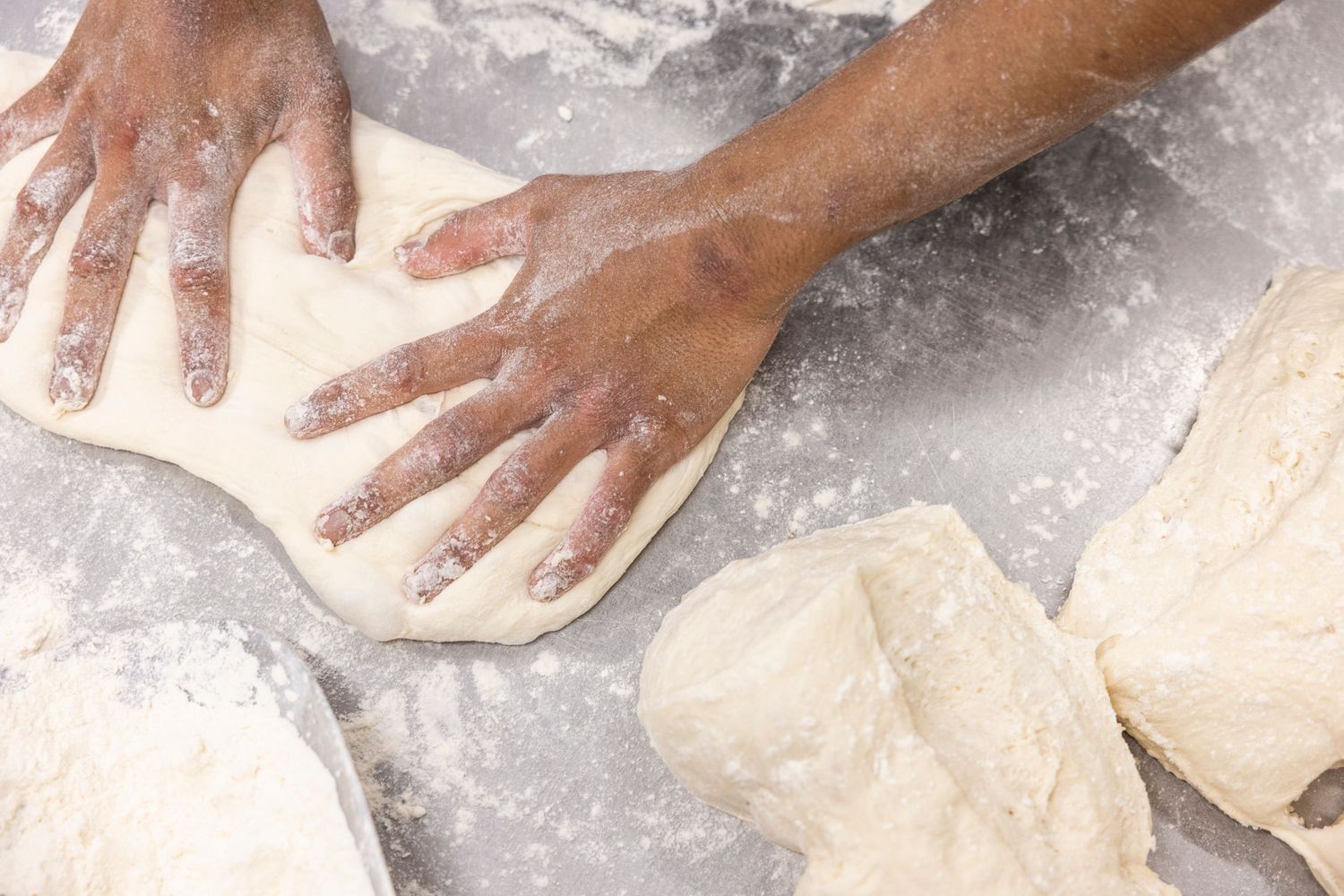 Hands kneading white dough on a floured surface in rustic kitchen setting.