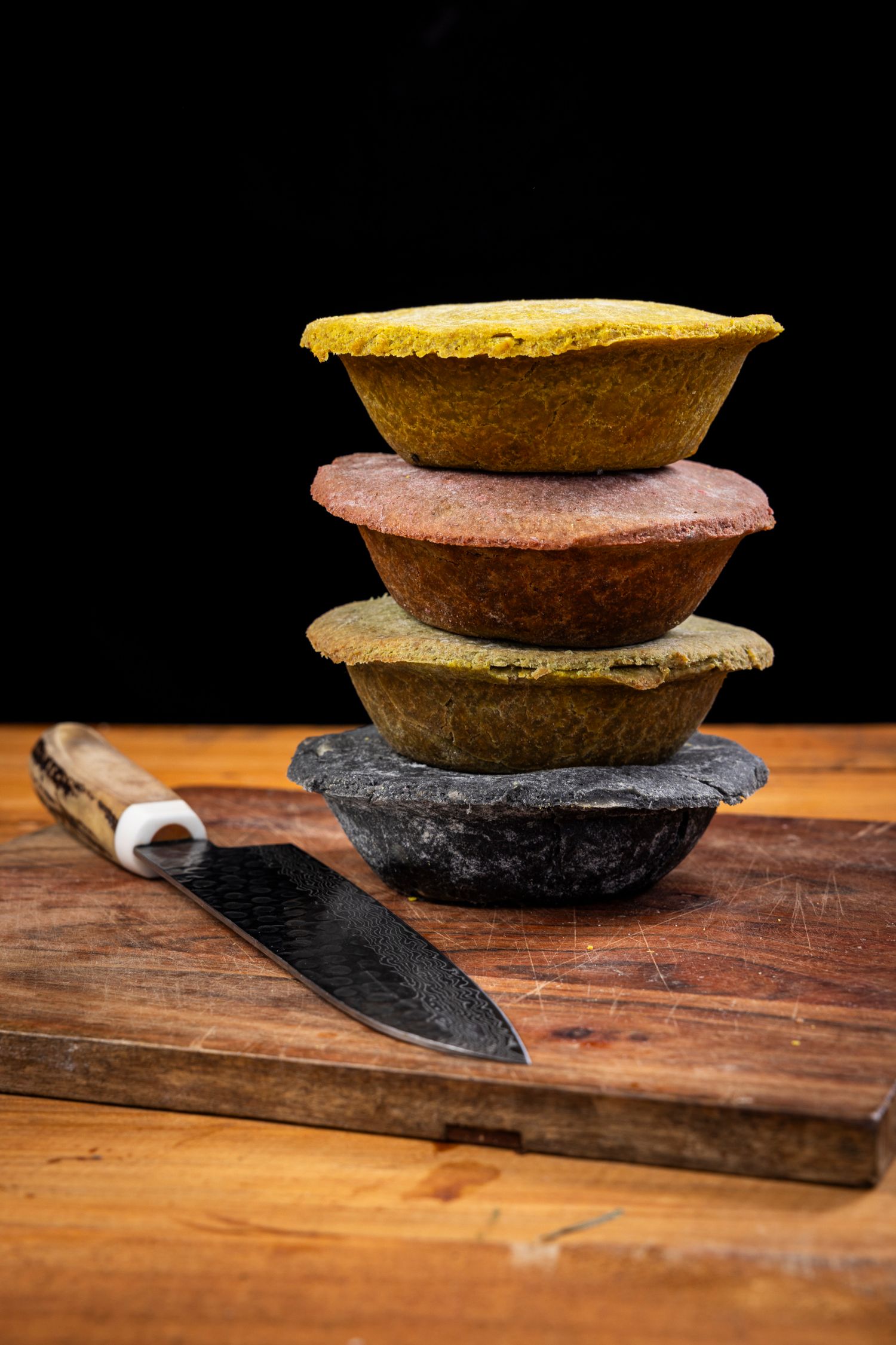 Homemade pies displayed on black stone plates against a wooden cutting board background.