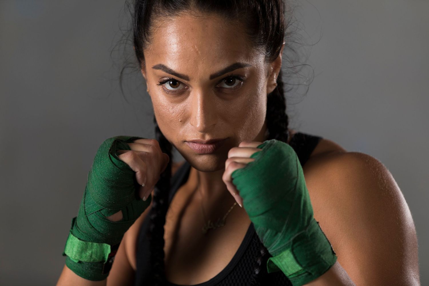 A boxer poses in fighting stance wearing green hand wraps against a dark background.