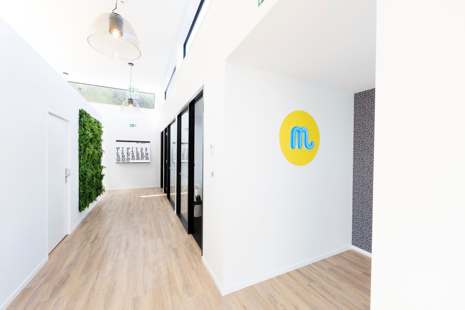 Minimalist office hallway with living wall feature and yellow circular logo.
