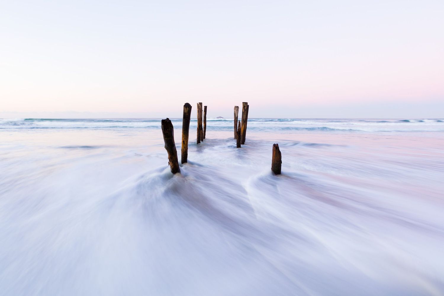 Weathered wooden pilings stand silently in smooth snowy beach landscape at dusk.