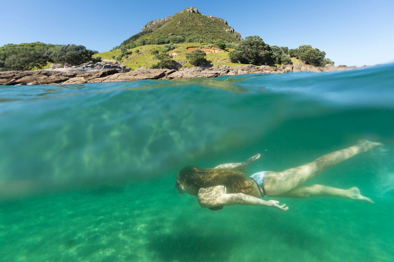Underwater view of turquoise waters near a rocky coastline with clear visibility.