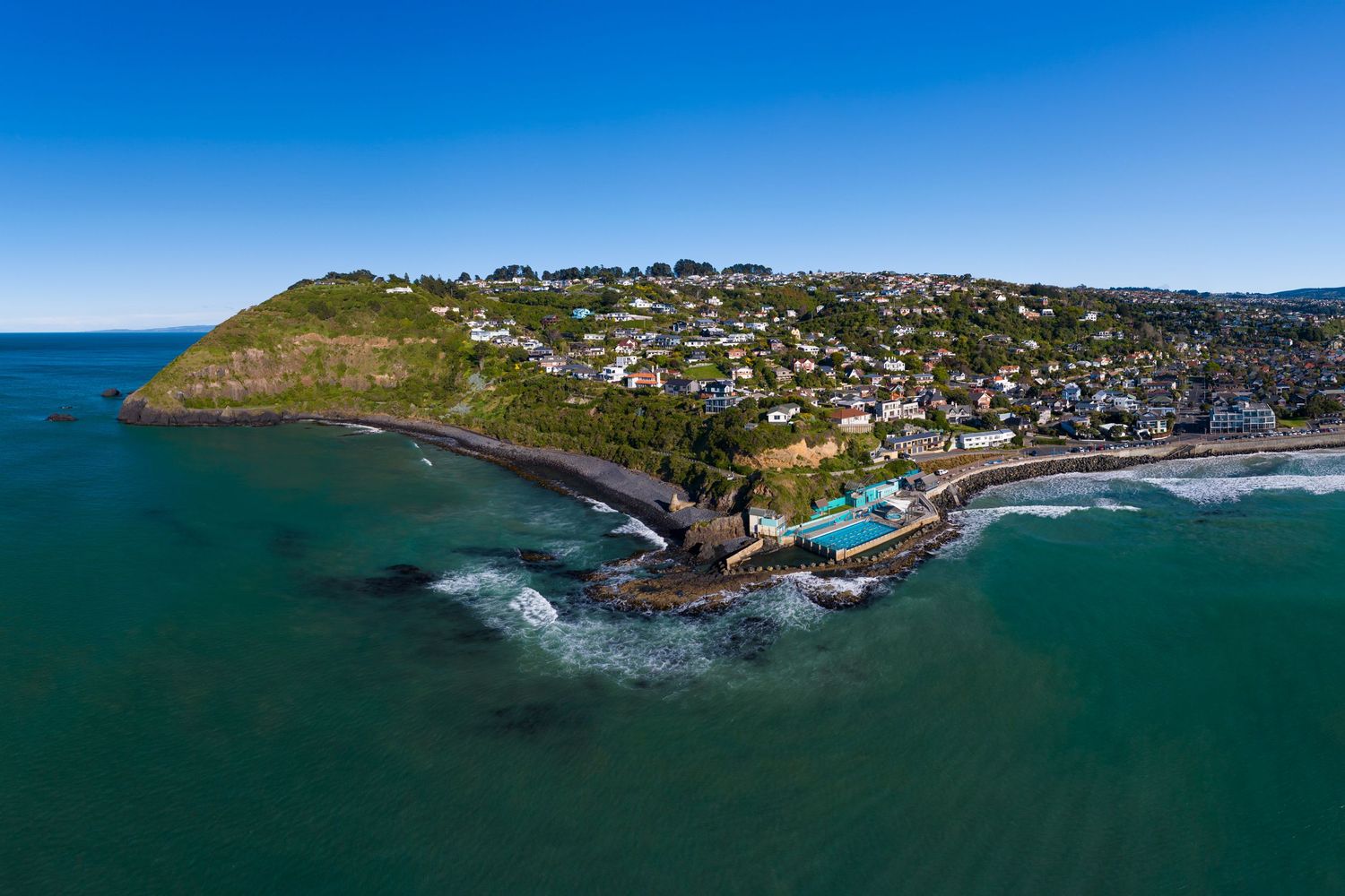 Aerial coastal panorama shows rugged cliffs and seaside community nestled along turquoise waters.