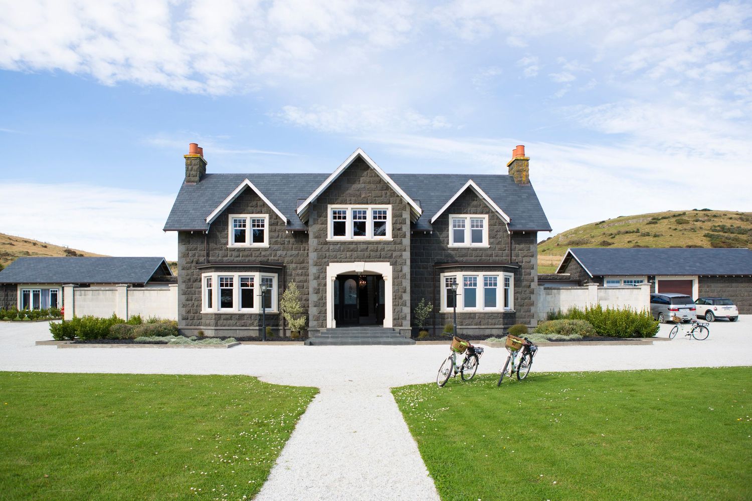 Large grey stone house with symmetrical design and manicured lawn featuring a central walkway.