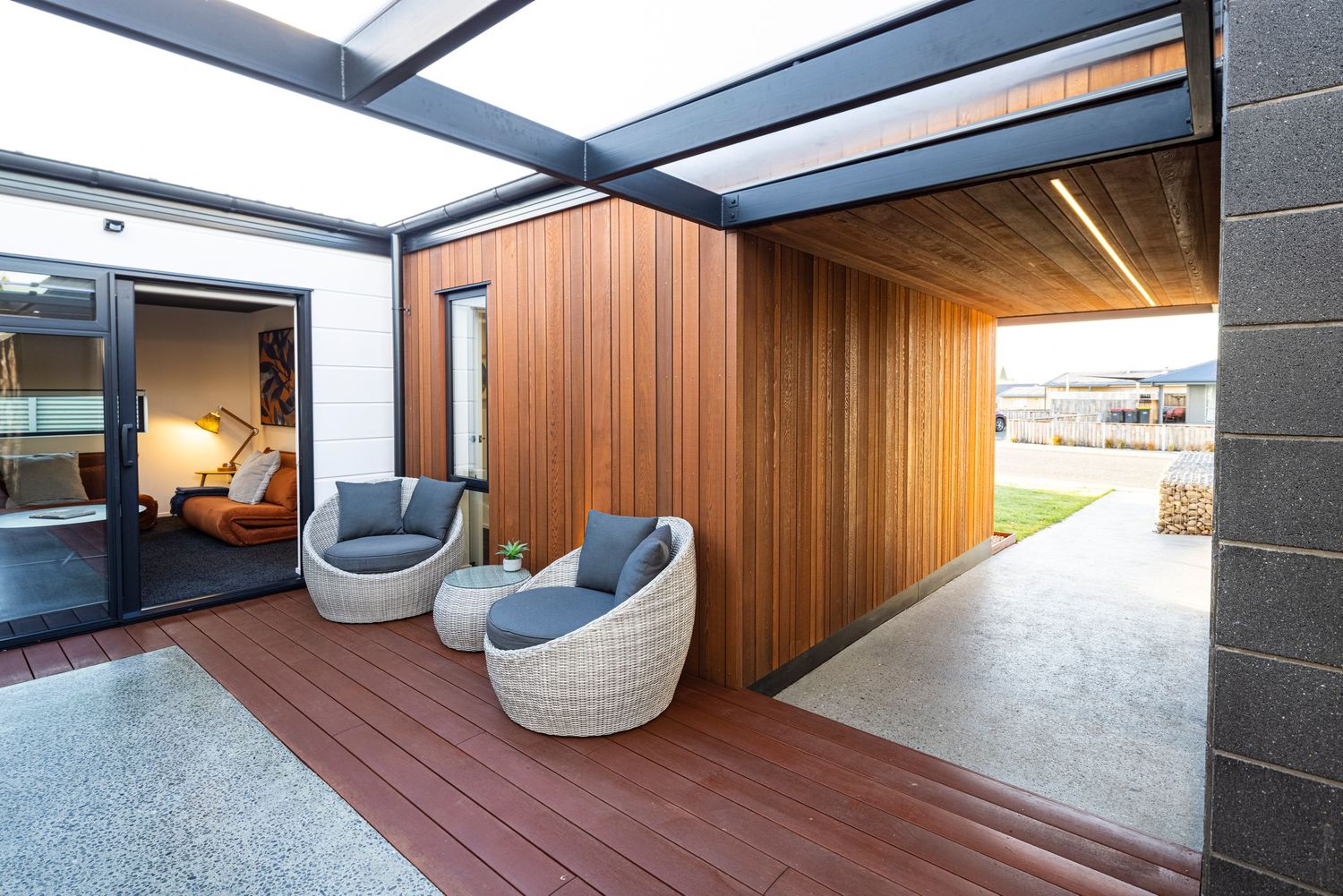 Modern outdoor patio area with woven chairs and wood paneled walls.