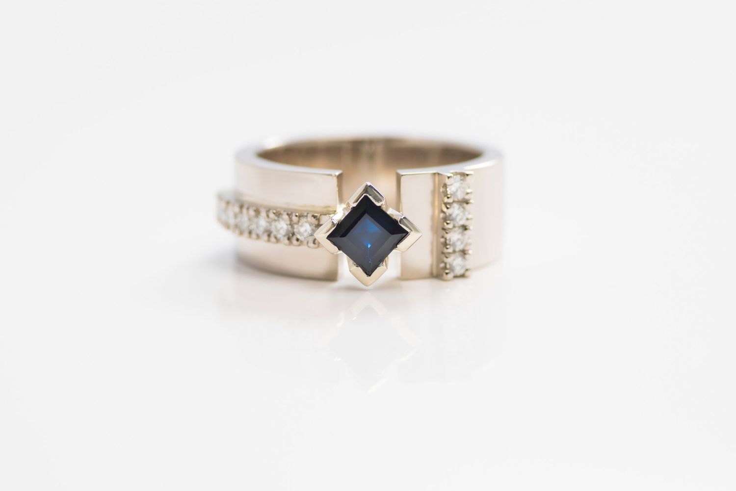 Modern silver ring with square blue gemstone and diamond accents on white background.