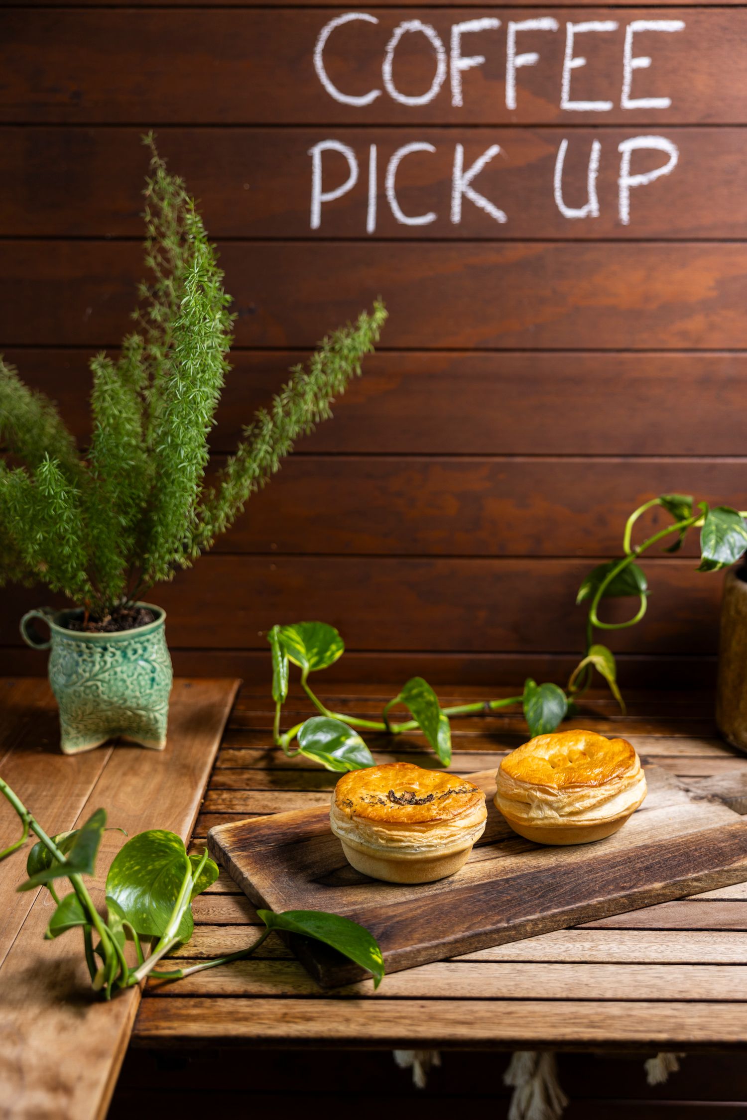 Coffee pickup area with wooden walls, potted plants and pastries on rustic table.