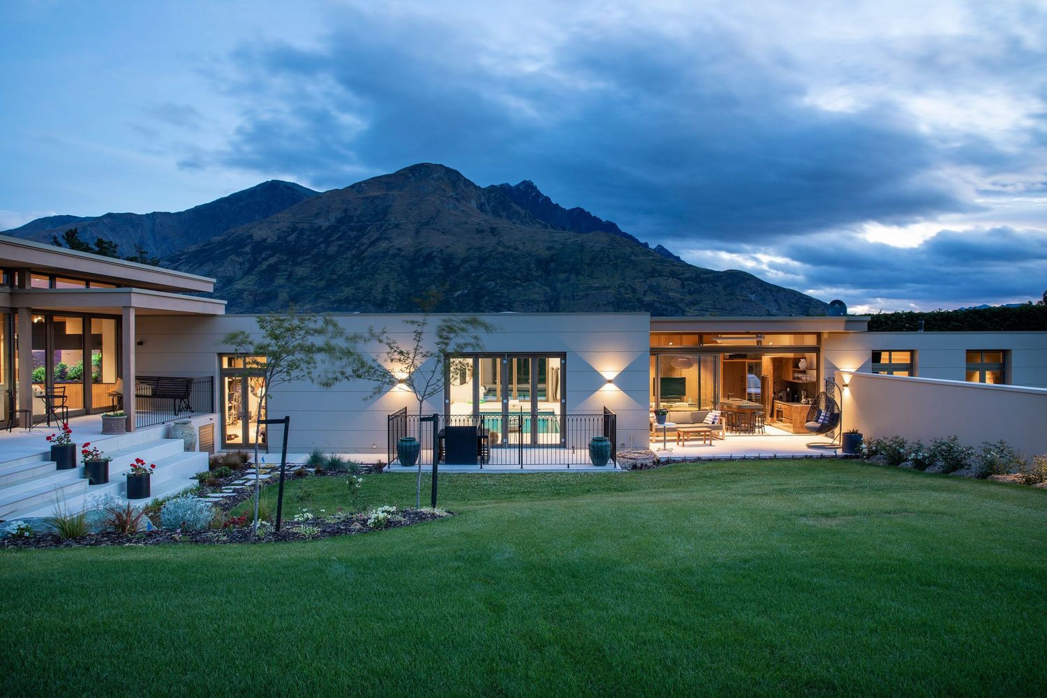 Modern mountain home exterior at dusk with dramatic lighting and scenic backdrop.