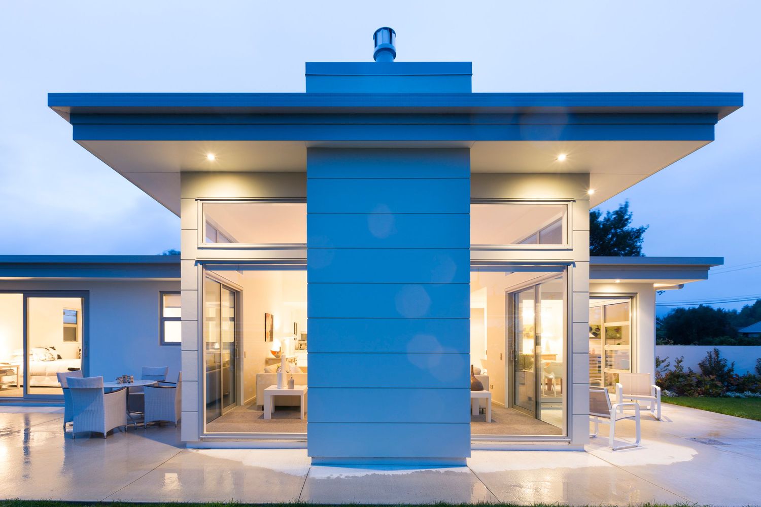 Modern blue and white house exterior with large glass windows and flat roof design.