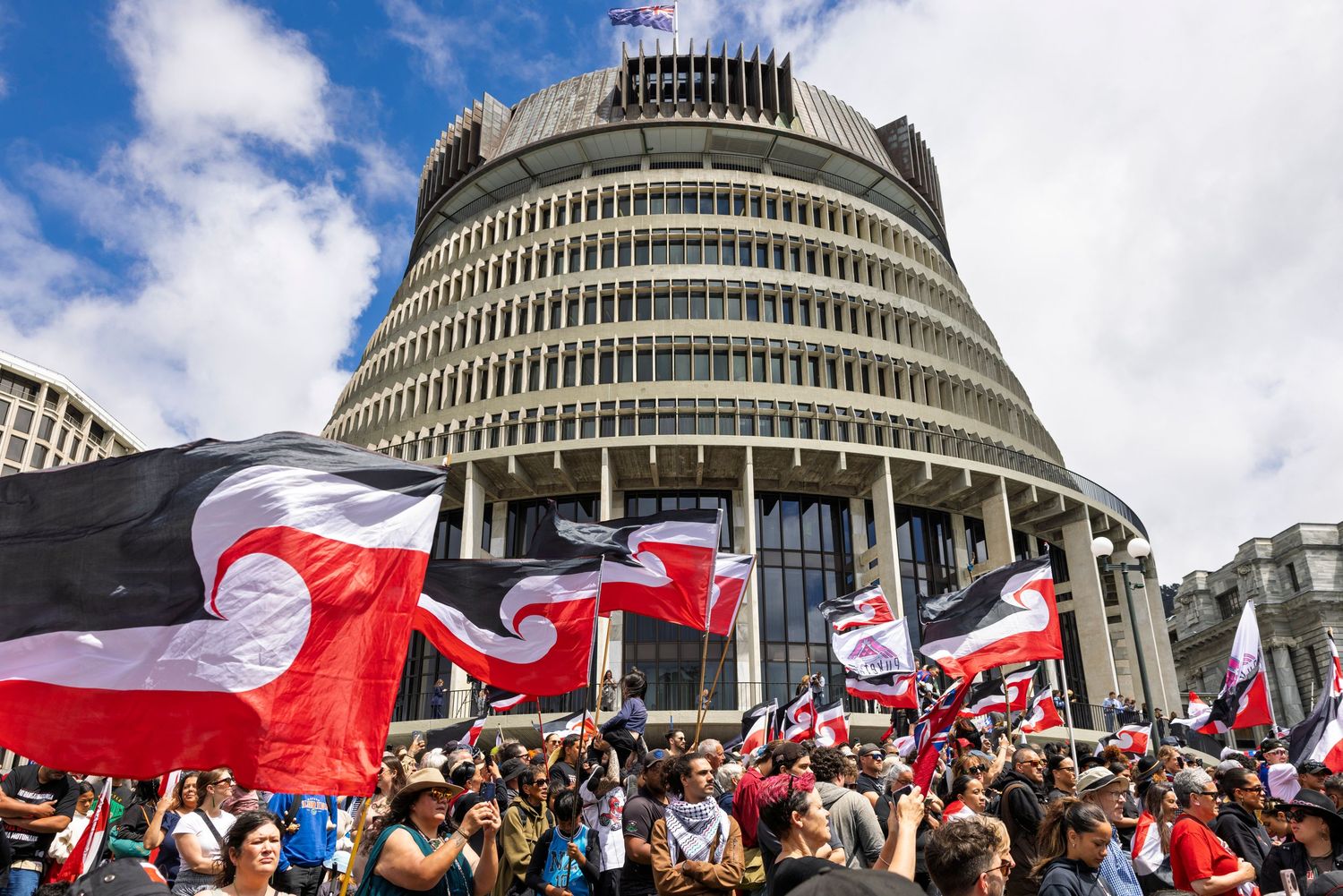 Large crowd gathered outside government building with red and white flags waving.