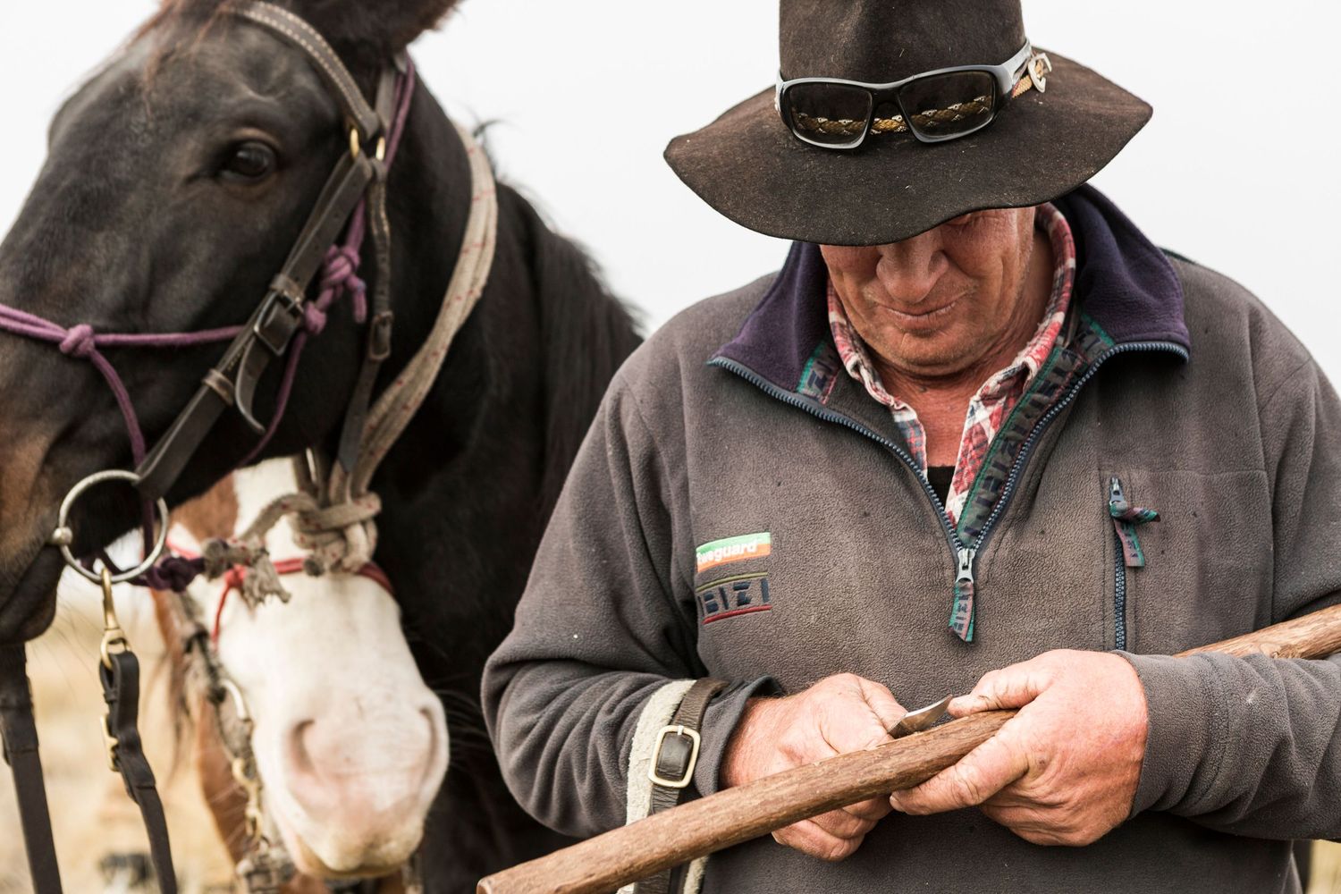 Close-up of handler checking horse's equipment while wearing traditional countryside attire.