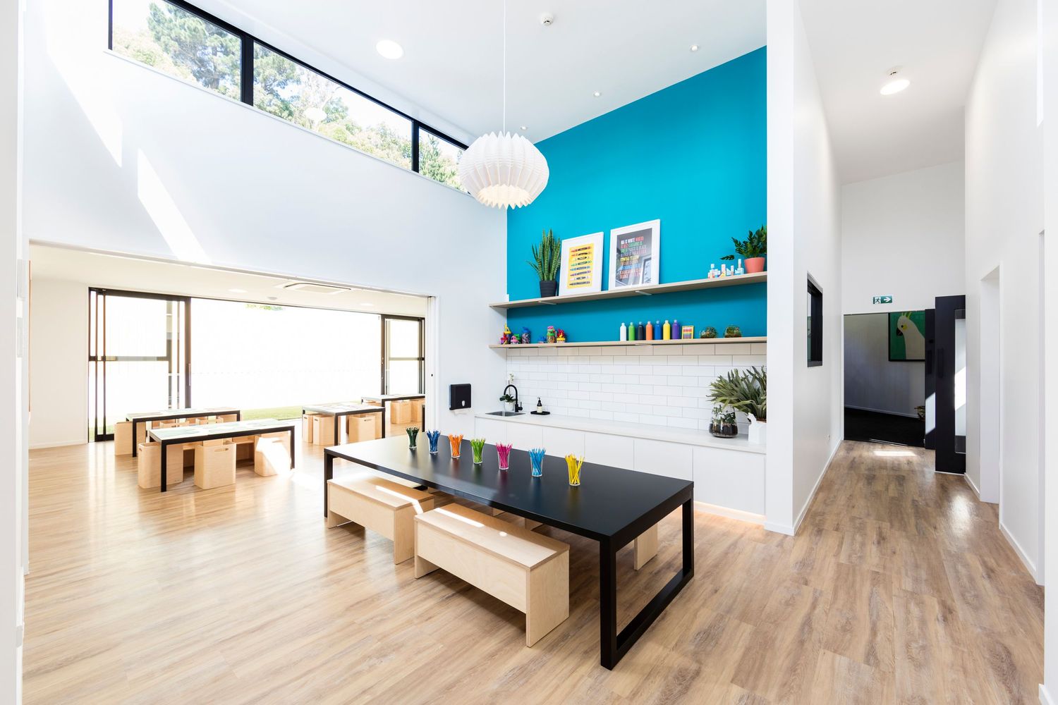 Modern break room with turquoise accent wall, wooden benches, and high ceilings.