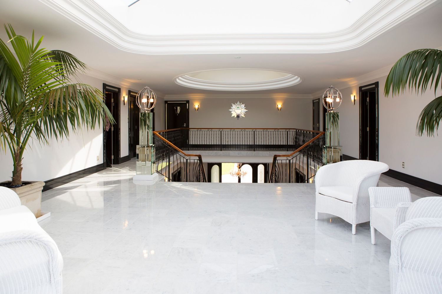 Luxurious white lobby with skylight, palm trees, and contemporary white furniture.