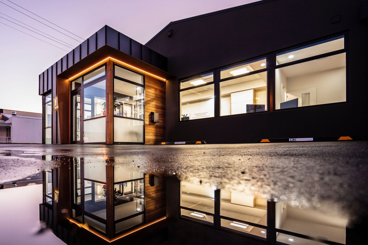 Contemporary home exterior with warm interior lighting glowing through expansive windows at dusk.