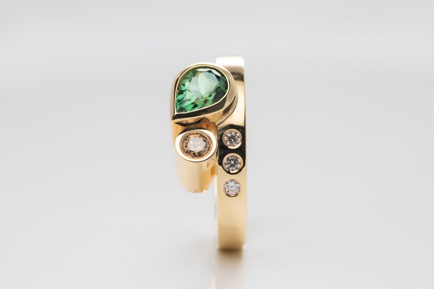 Gold ring featuring teardrop-shaped green gemstone and diamond accents on light background.