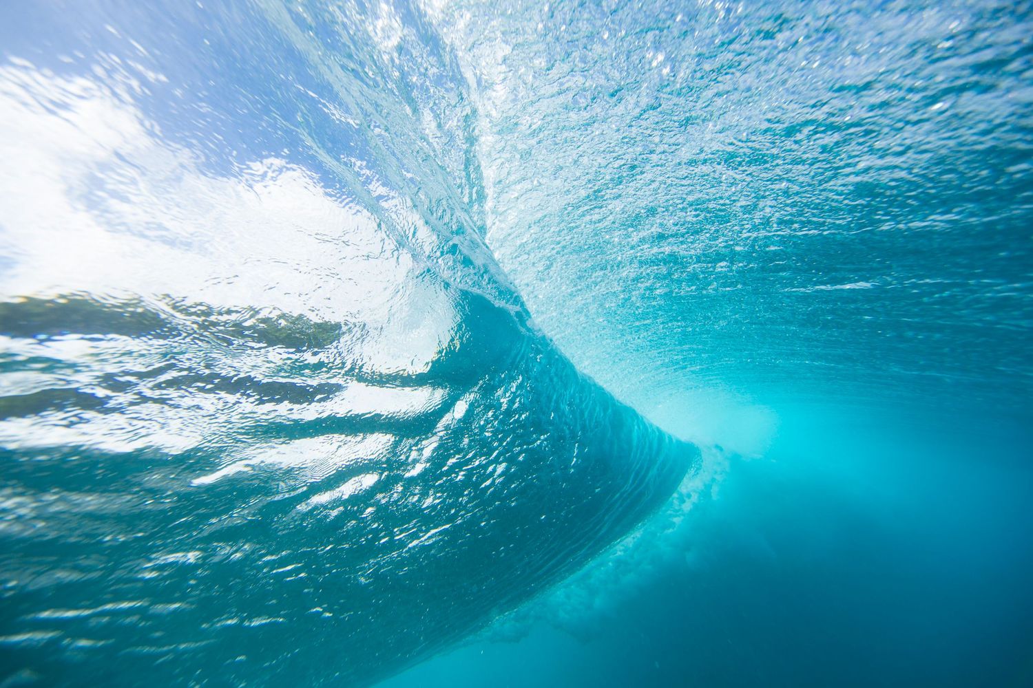 Underwater view of a crystal clear ocean wave breaking with sunlight filtering through.