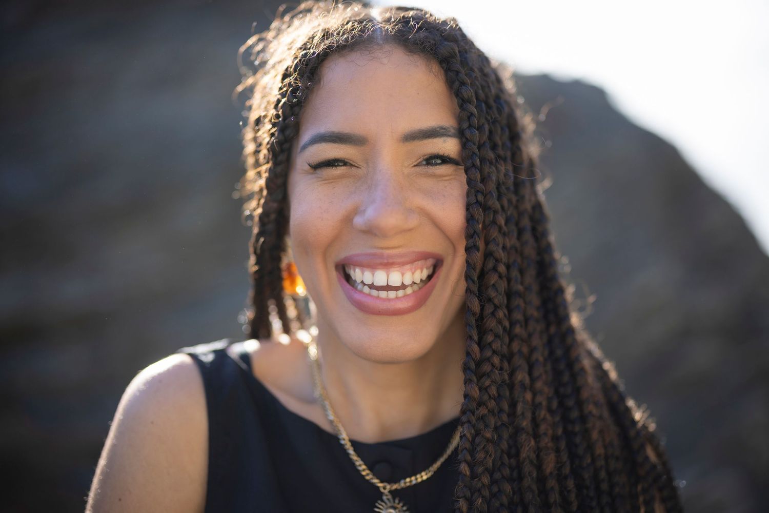 Natural portrait shot with braided hair against outdoor coastal background.