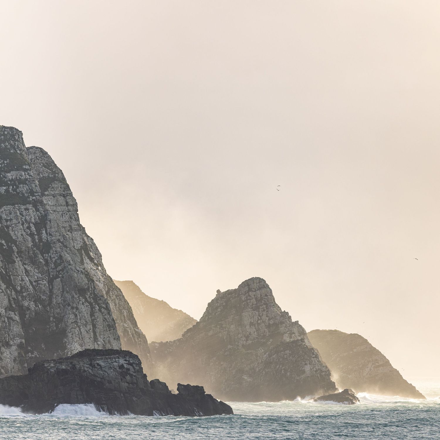 Dramatic coastal landscape with rocky cliffs emerging from misty ocean waters.