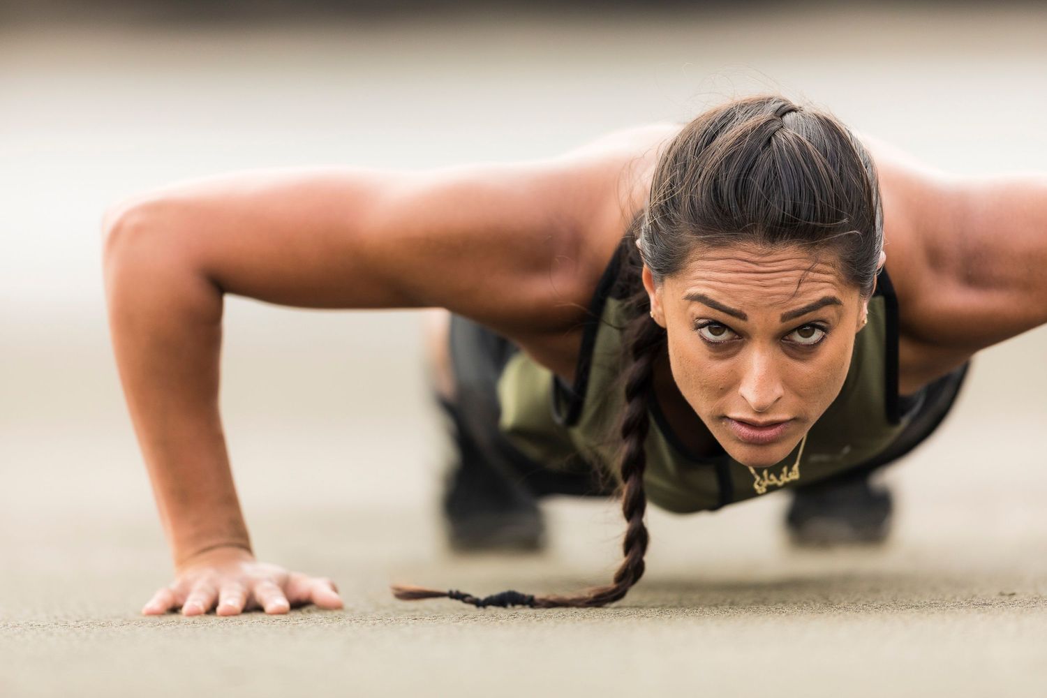 An athlete performs a plank exercise position on a concrete surface showing intense focus and determination.