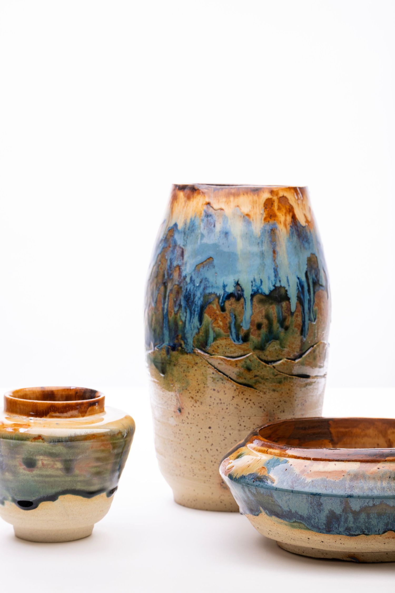 Three ceramic pottery pieces featuring blue and orange drip glaze effects on white background.