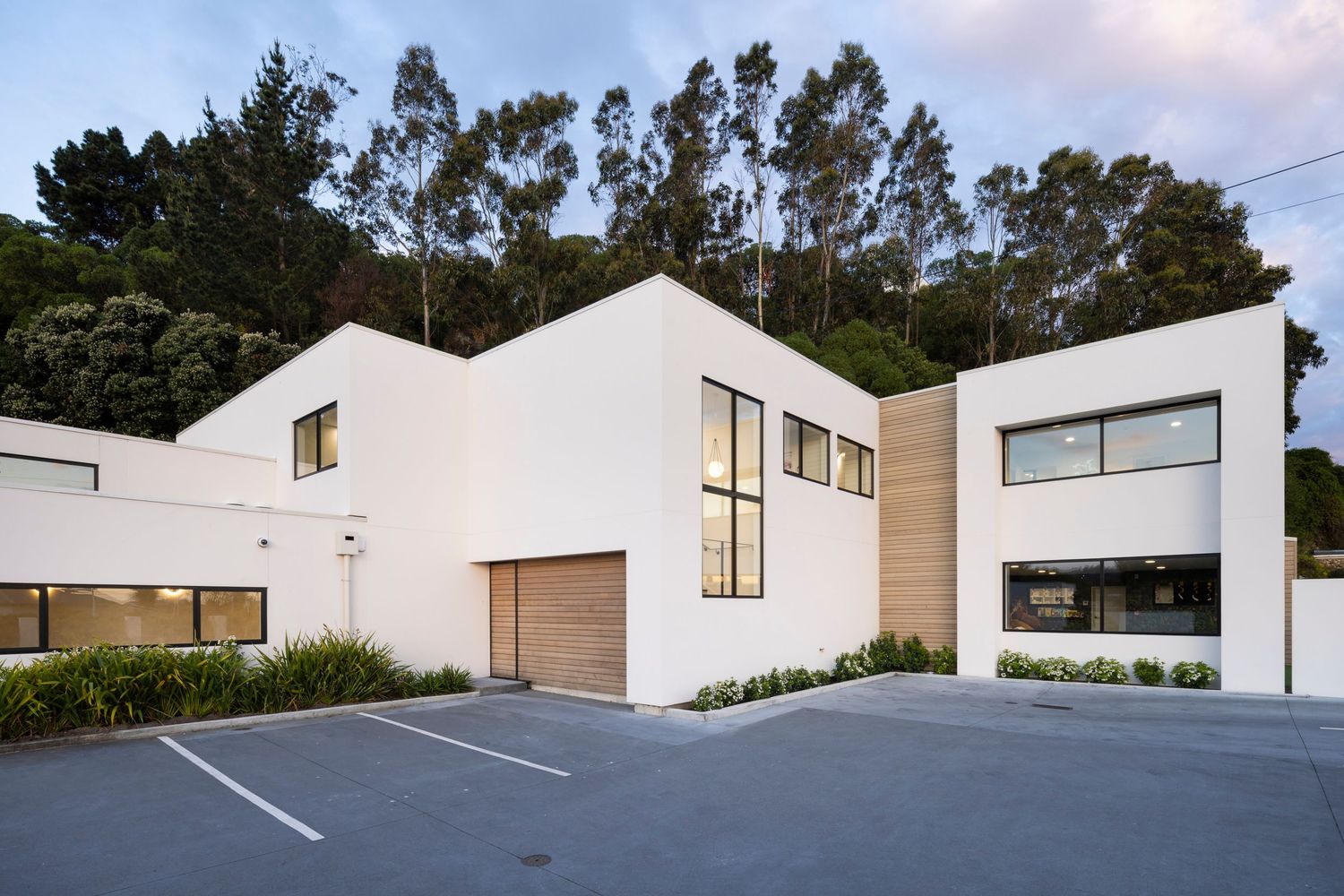 White commercial building with attached garage and parking area surrounded by trees.