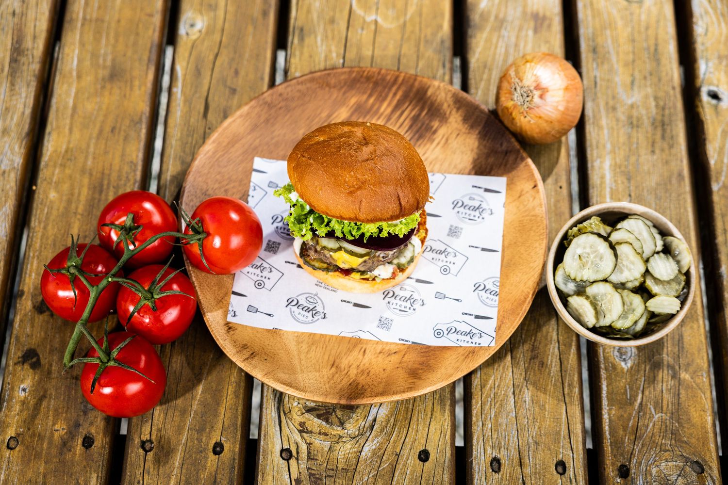 Fresh burger served on wooden board with vine tomatoes and pickles on rustic wooden table.
