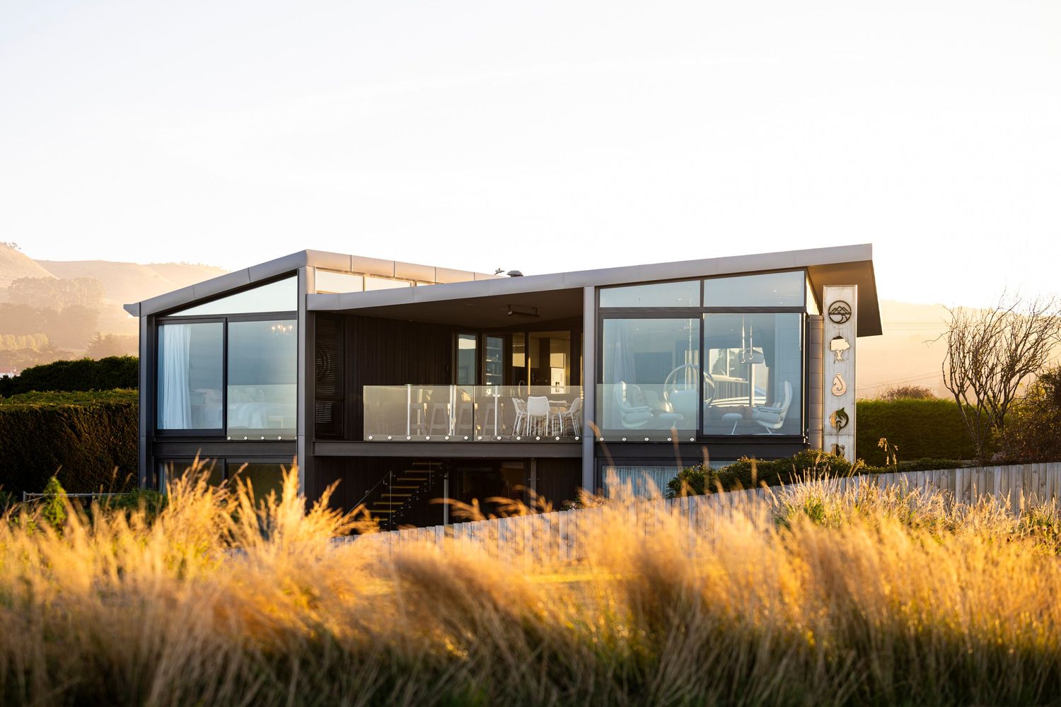 Modern glass house with deck surrounded by golden ornamental grasses.