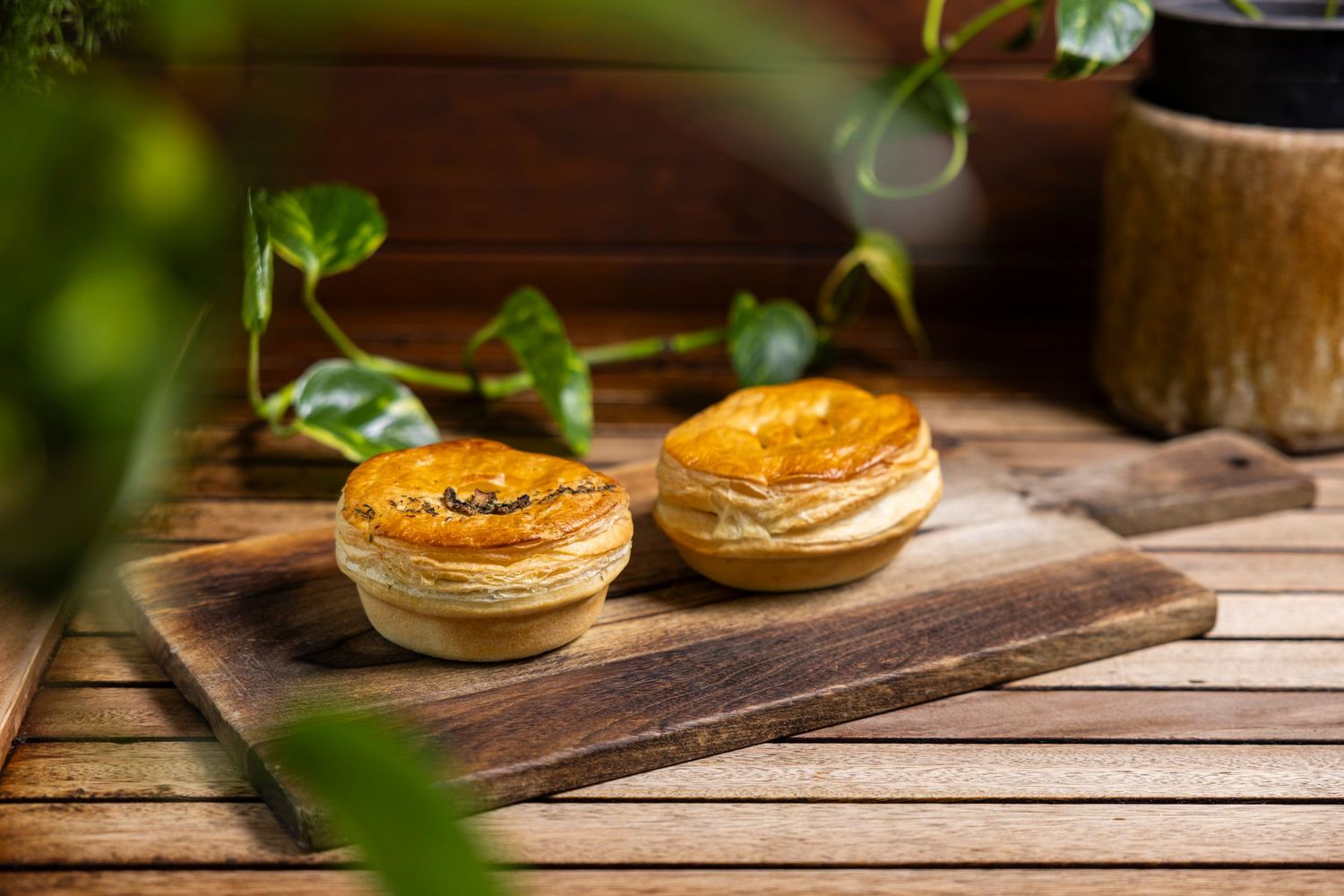 Two golden pies on wooden serving board with soft natural lighting.