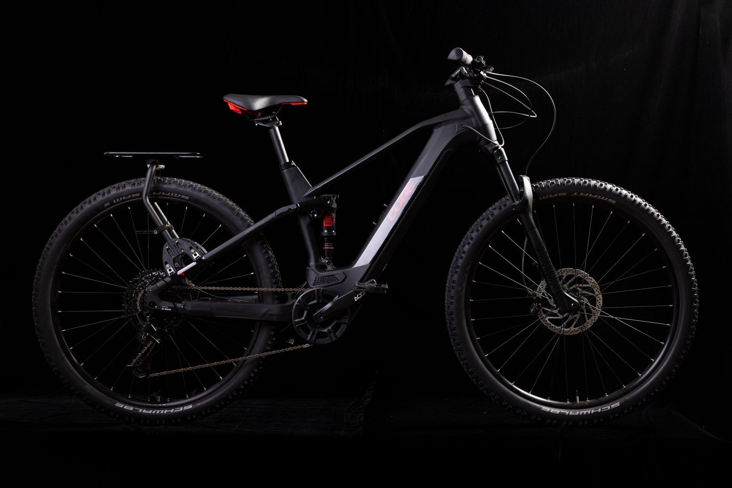 Side view of sleek black electric mountain bike with professional lighting against dark background.