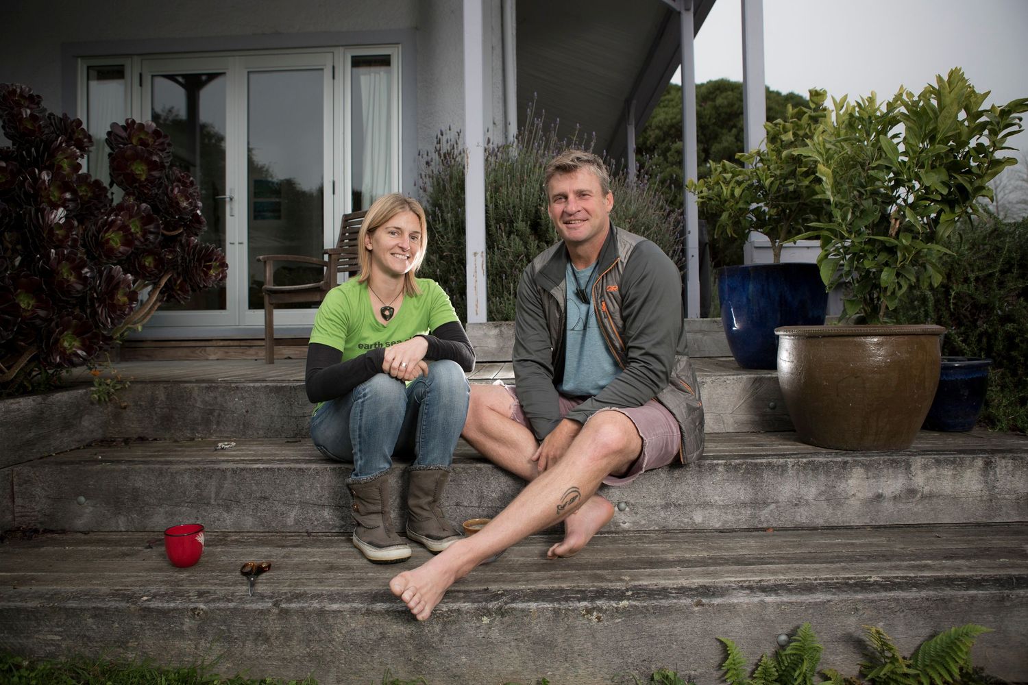 Two people relaxing on concrete steps outside a modern home with a red cup.