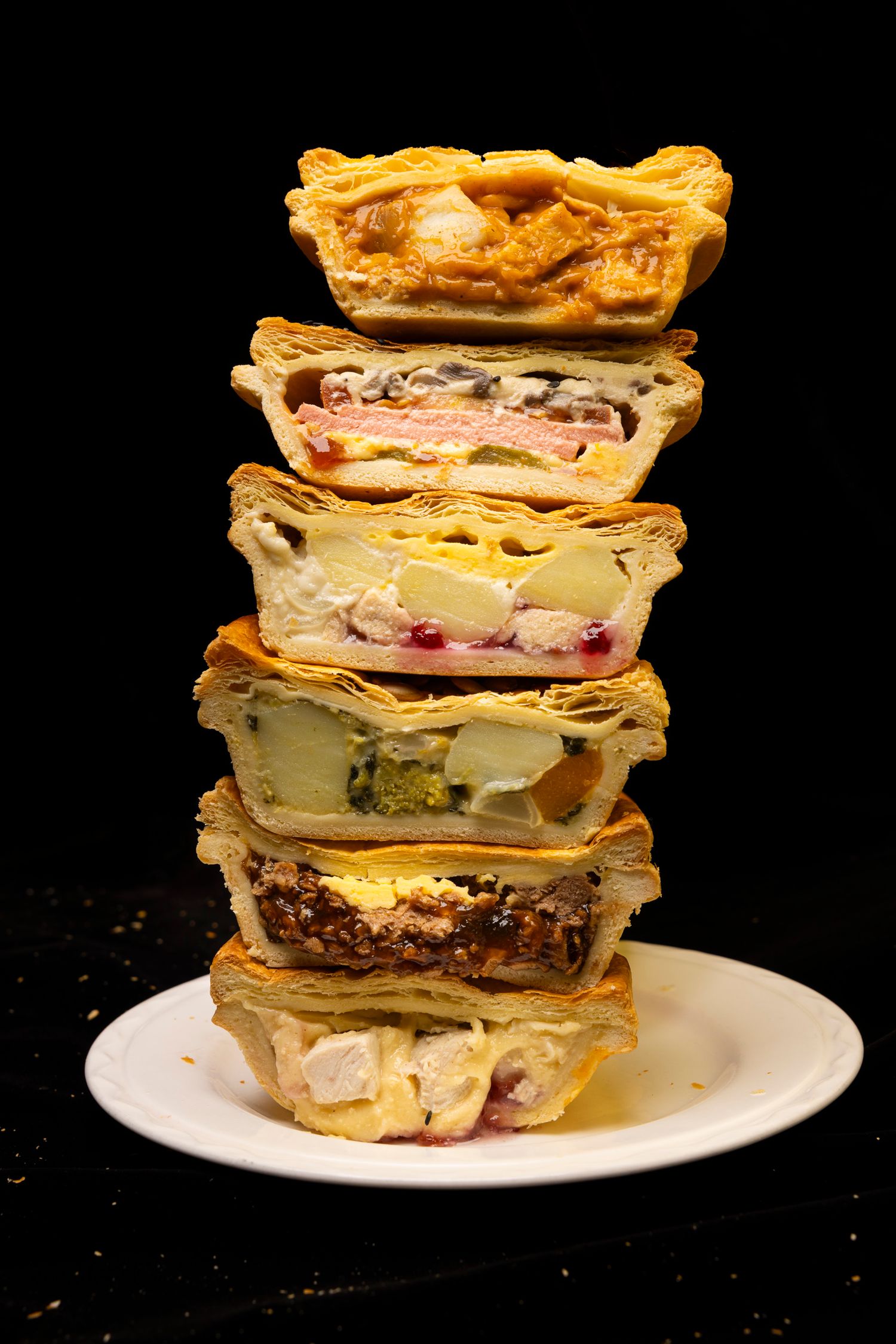 Stack of six different layered pies showcasing various fillings on white plate against black background.