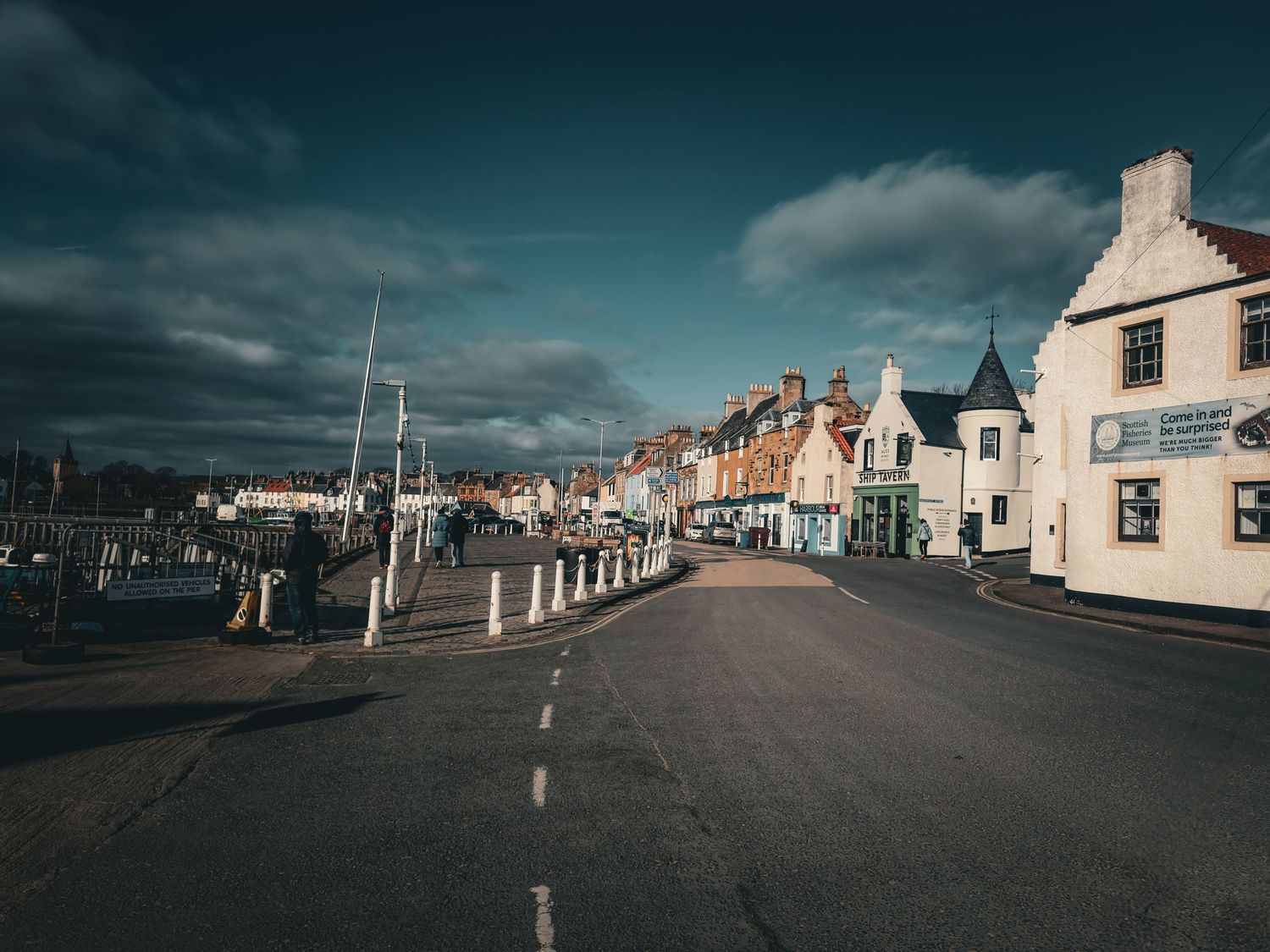 Quaint seaside town street lined with traditional Scottish buildings under moody sky.