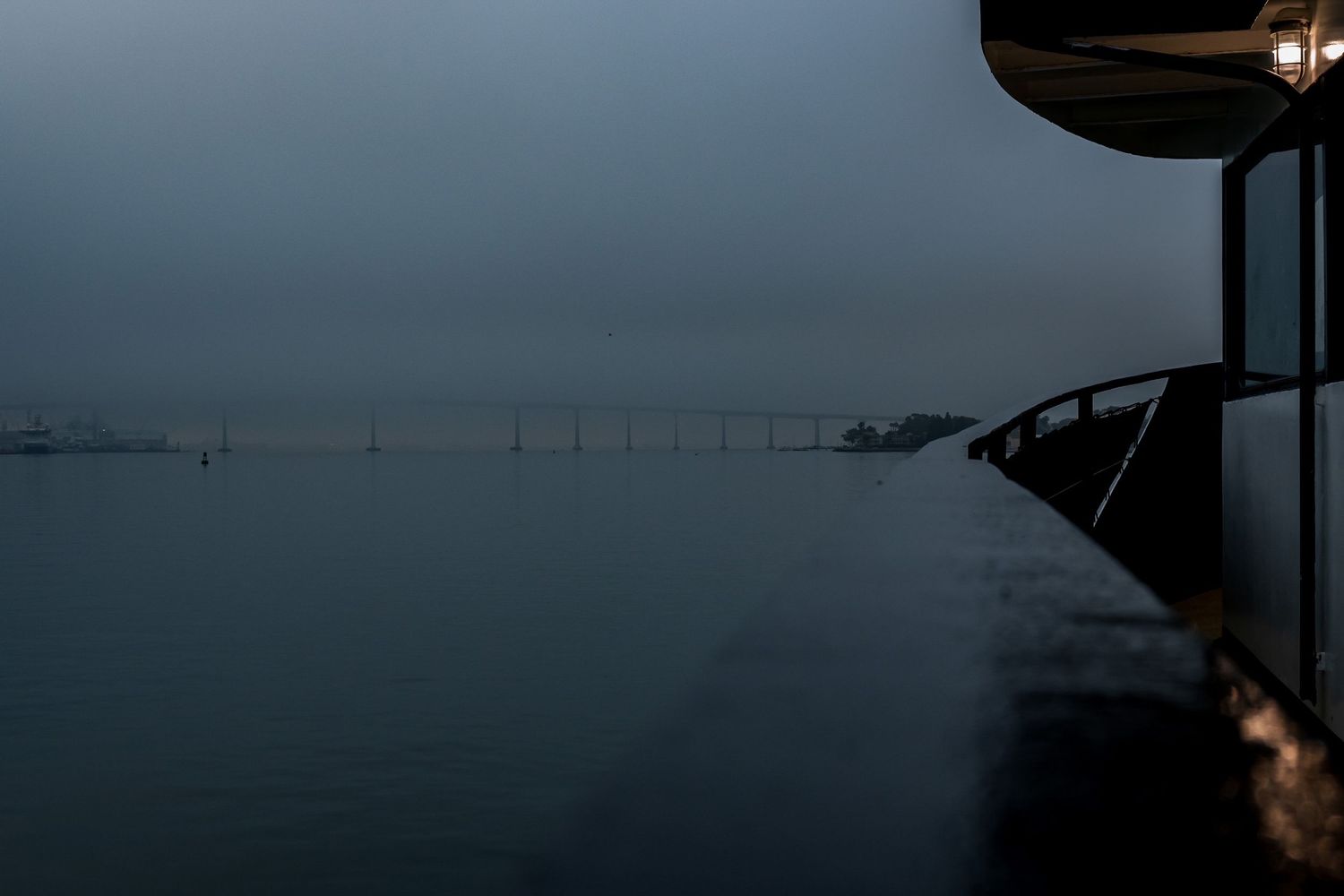 Misty waterfront view with distant bridge silhouetted against a gray horizon.