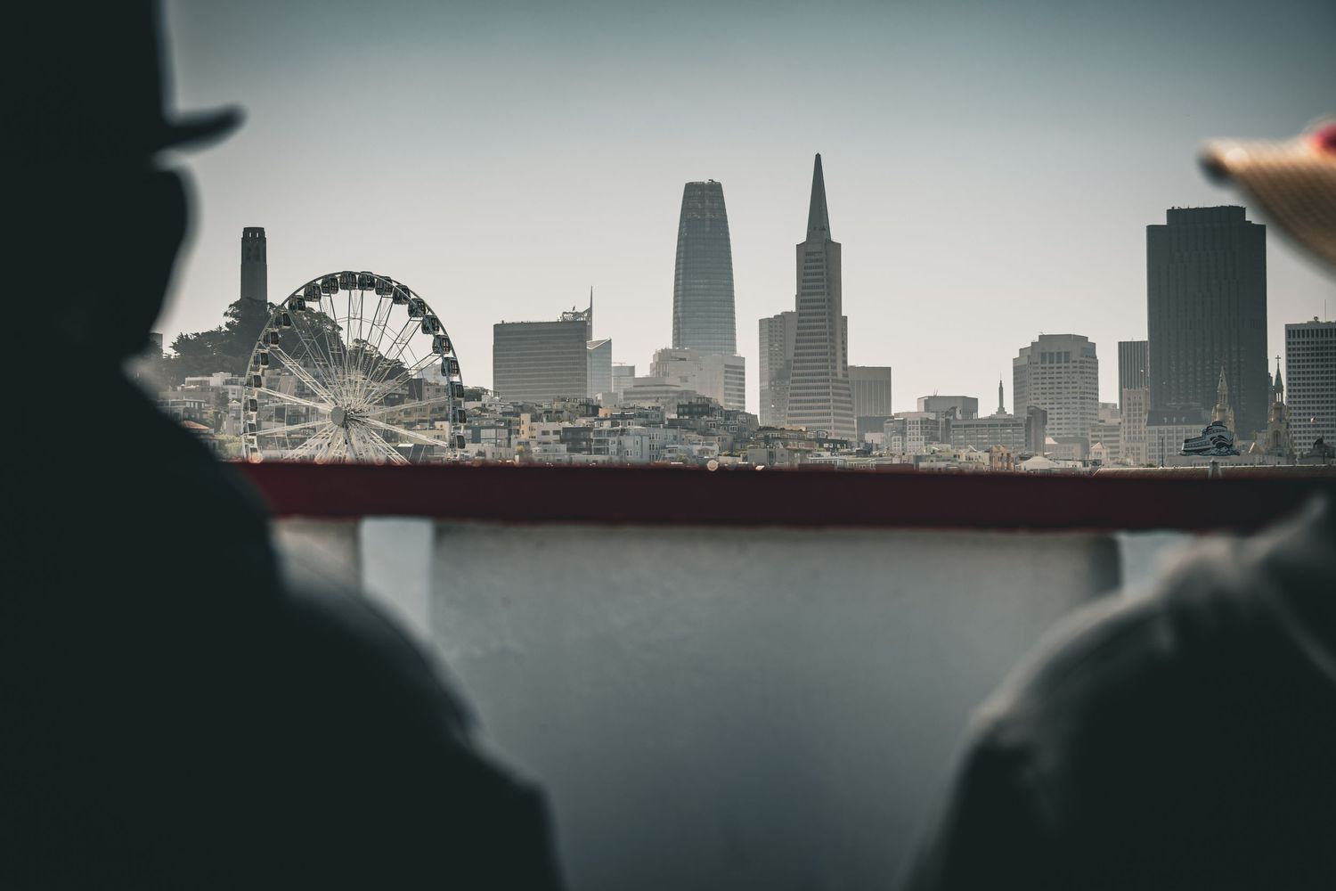 Silhouetted city skyline with Ferris wheel and skyscrapers visible through foggy conditions.