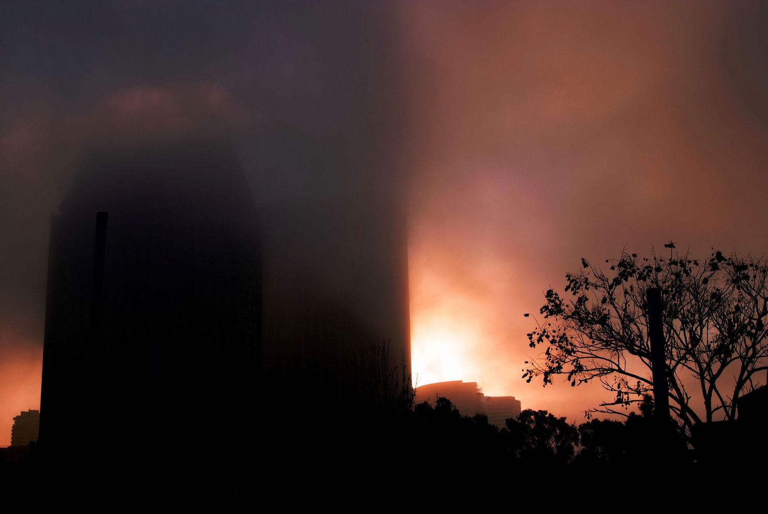 Dark silhouette of buildings against fiery orange sky at night.