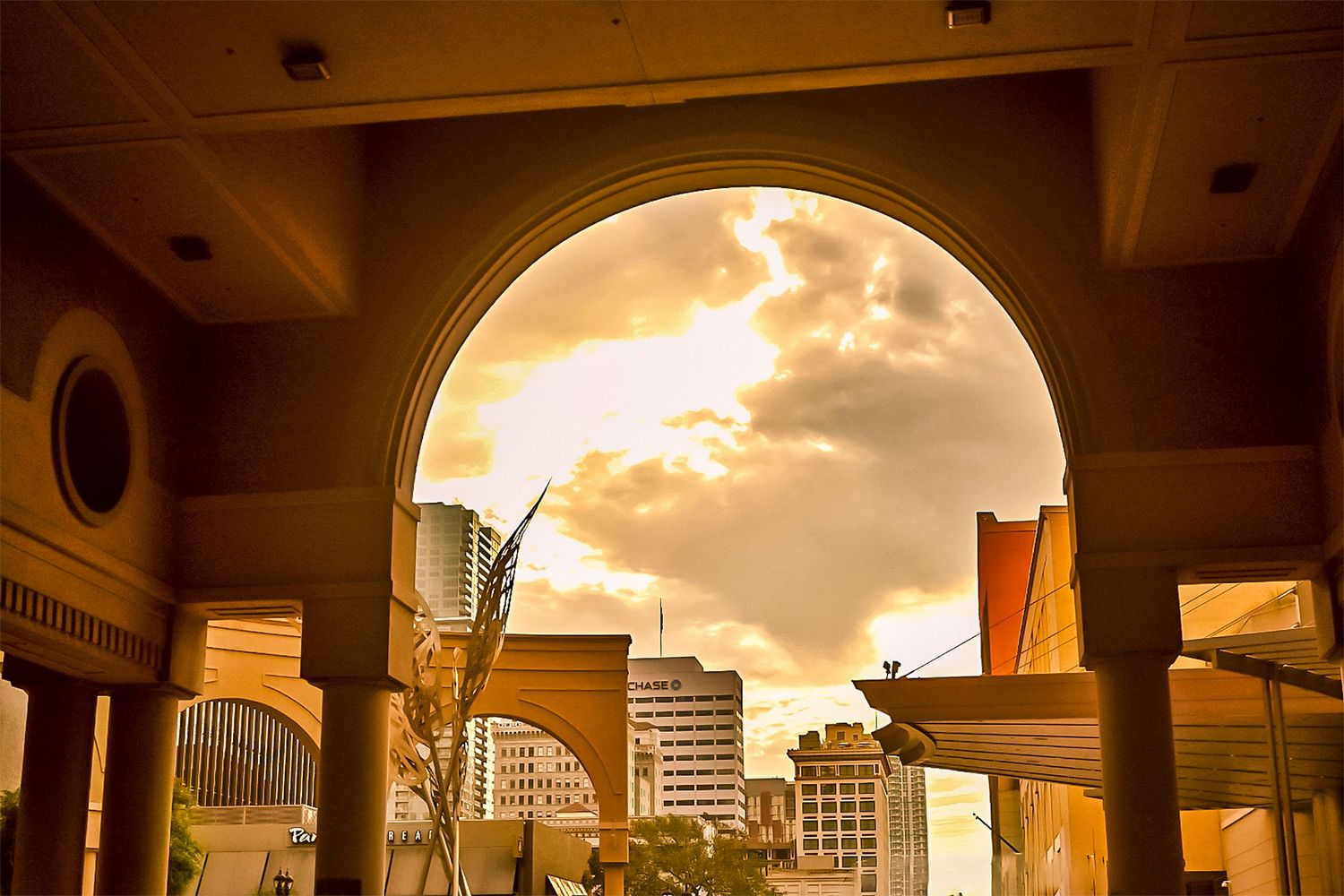 Arched interior walkway frames a dramatic cityscape and sunset through large windows.