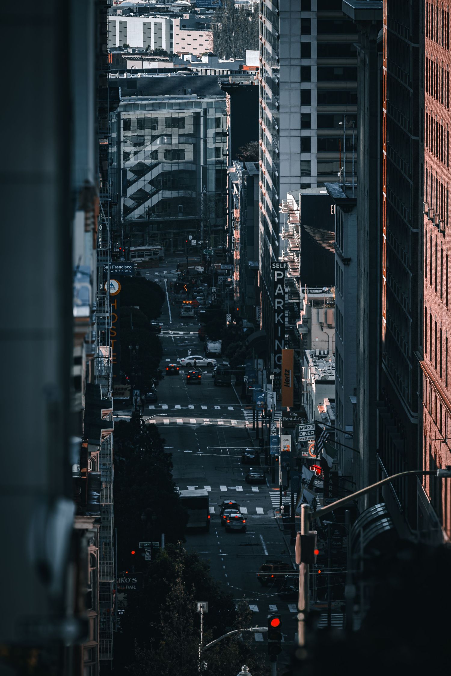 Aerial view looking down urban canyon of city street with tall buildings and traffic lights.