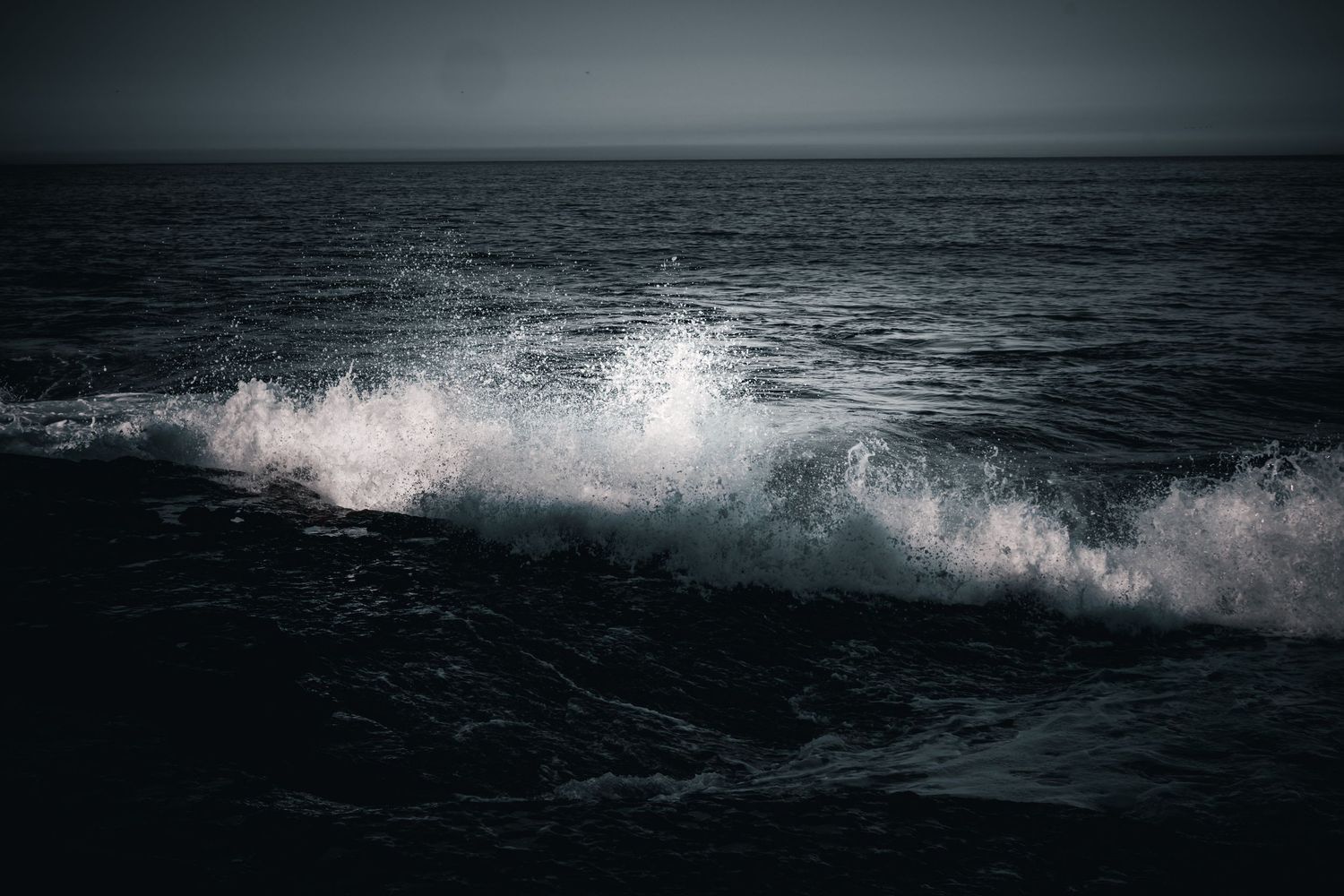 Dramatic ocean wave crashing and splashing in moody black and white seascape.
