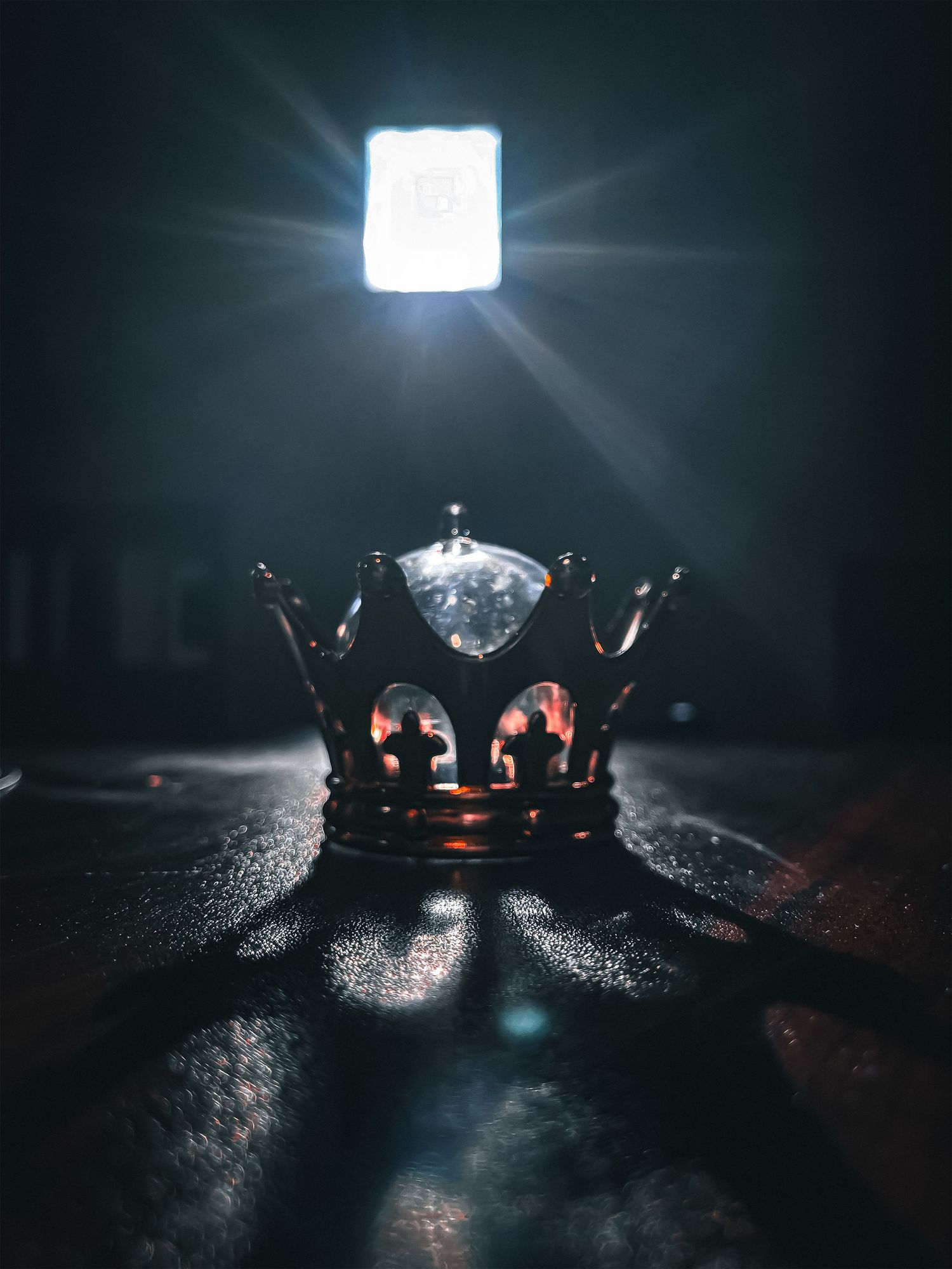 Dark metallic crown illuminated by bright overhead light creating dramatic shadows.