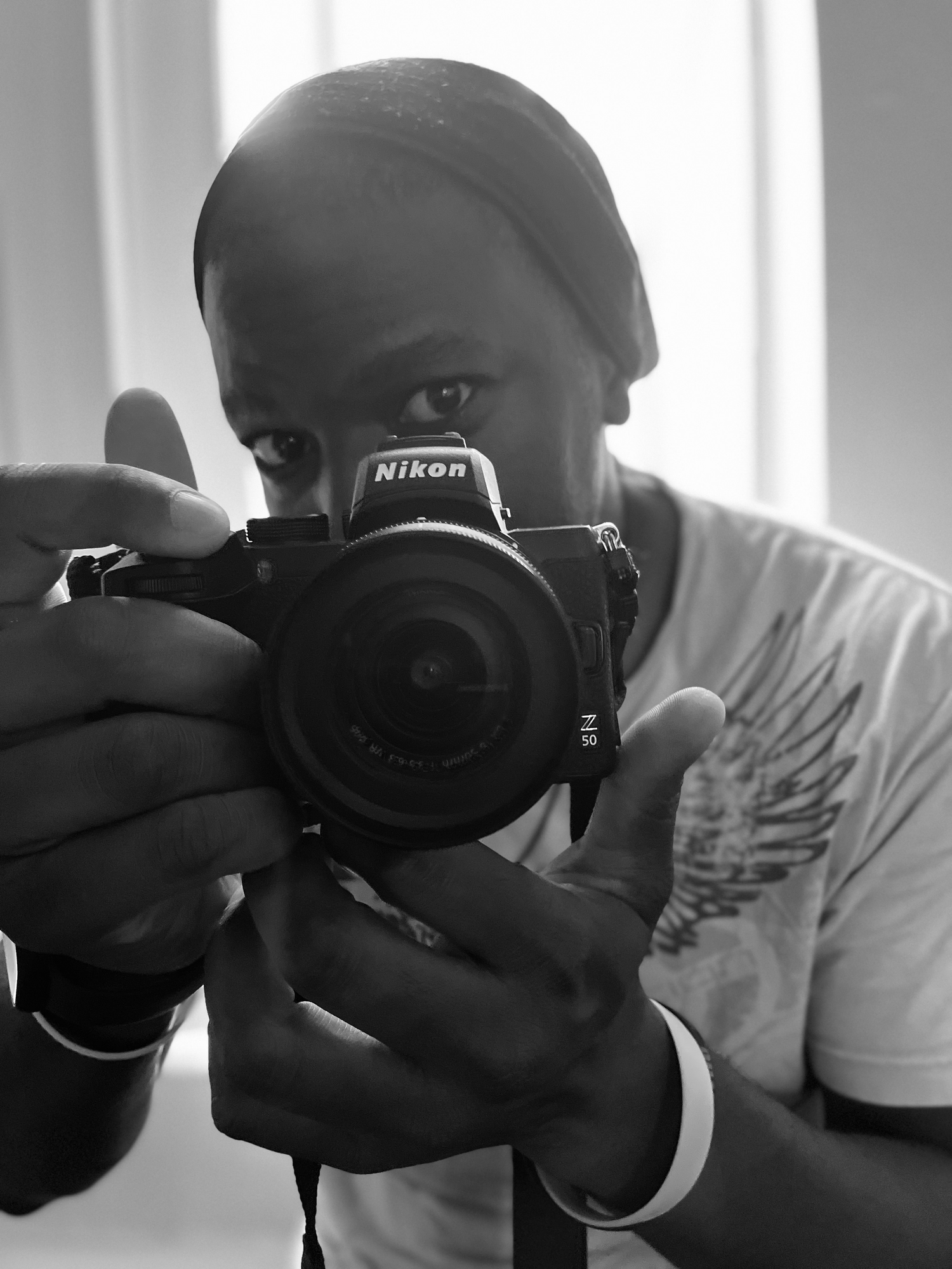 A photographer holding a Nikon camera takes a self-portrait in black and white.