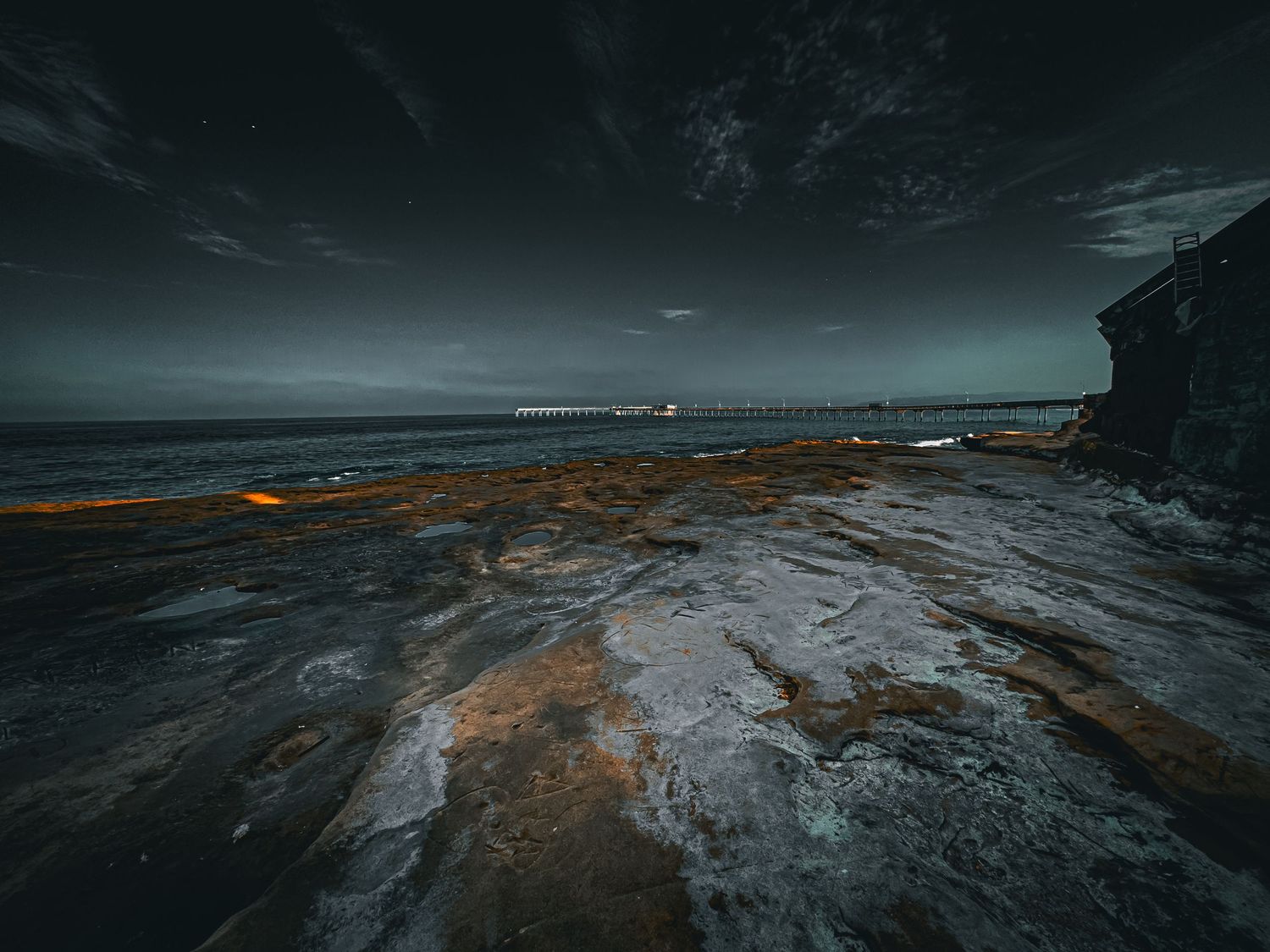 Dramatic coastal landscape at dusk with orange-tinted rocks and dark moody sky.